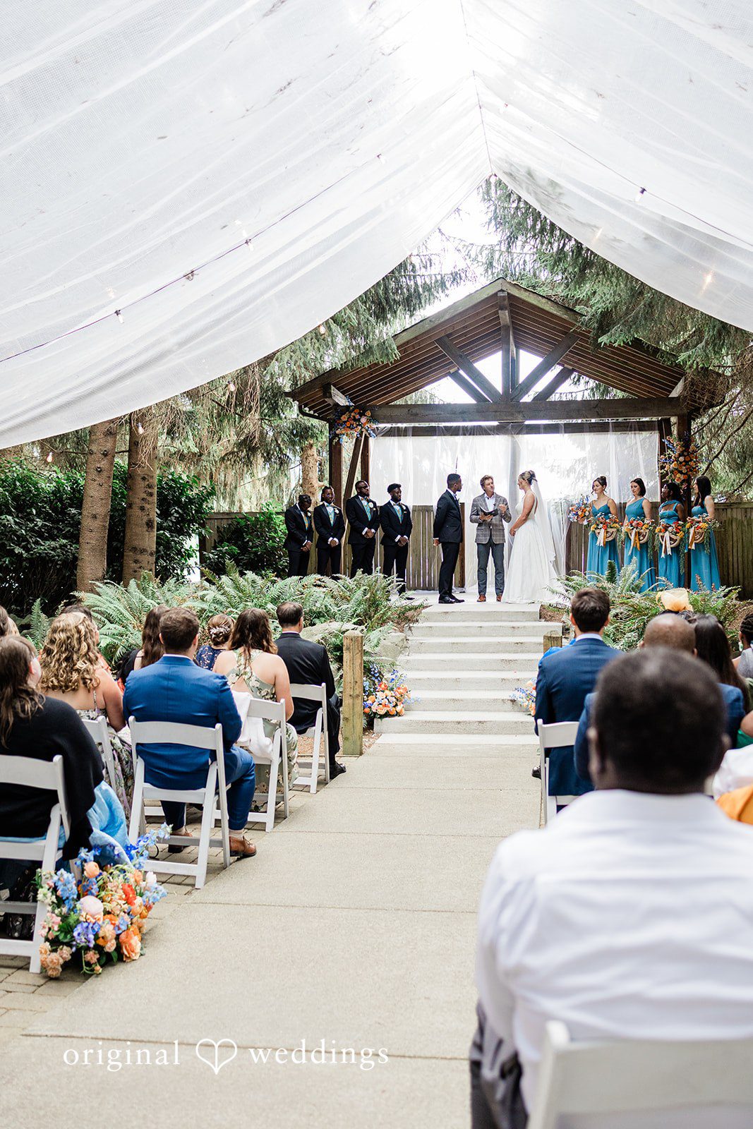 Katrina + Japhet Wedding guests seated on chairs watching a ceremony take place under an open-air structure.