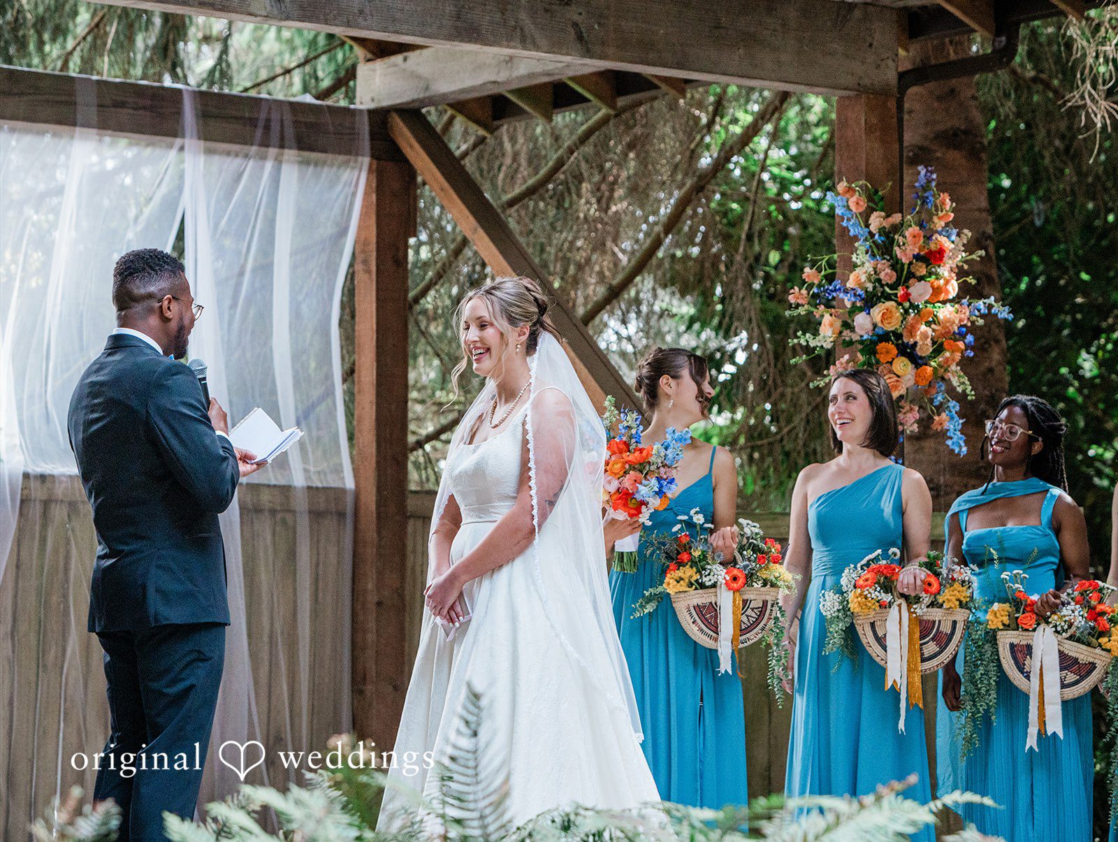 Katrina + Japhet Wedding party standing in a row next to a rustic wooden structure during the ceremony.
