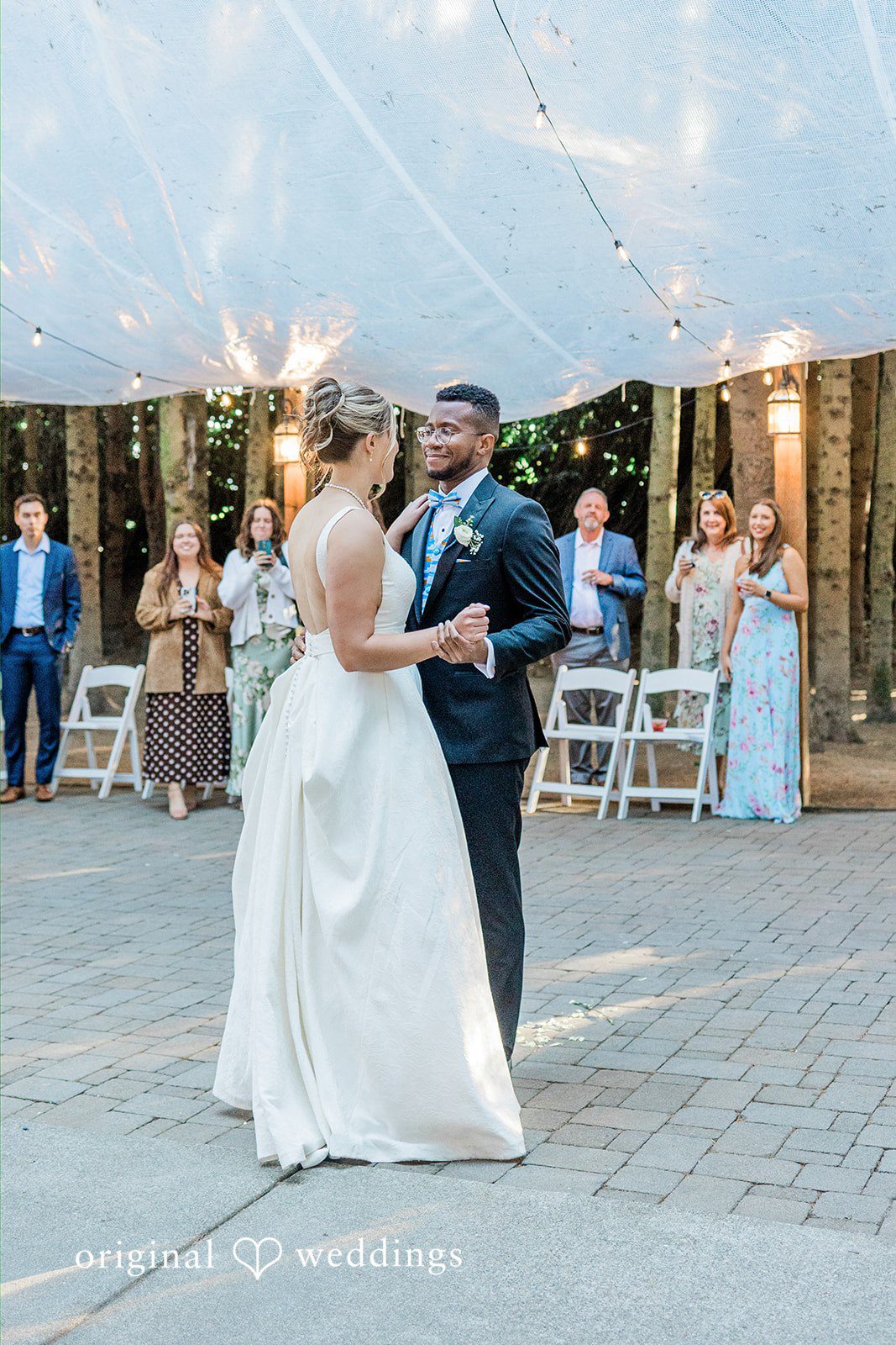 Katrina + Japhet Bride and groom sharing their first dance on a paved floor surrounded by seated wedding guests.
