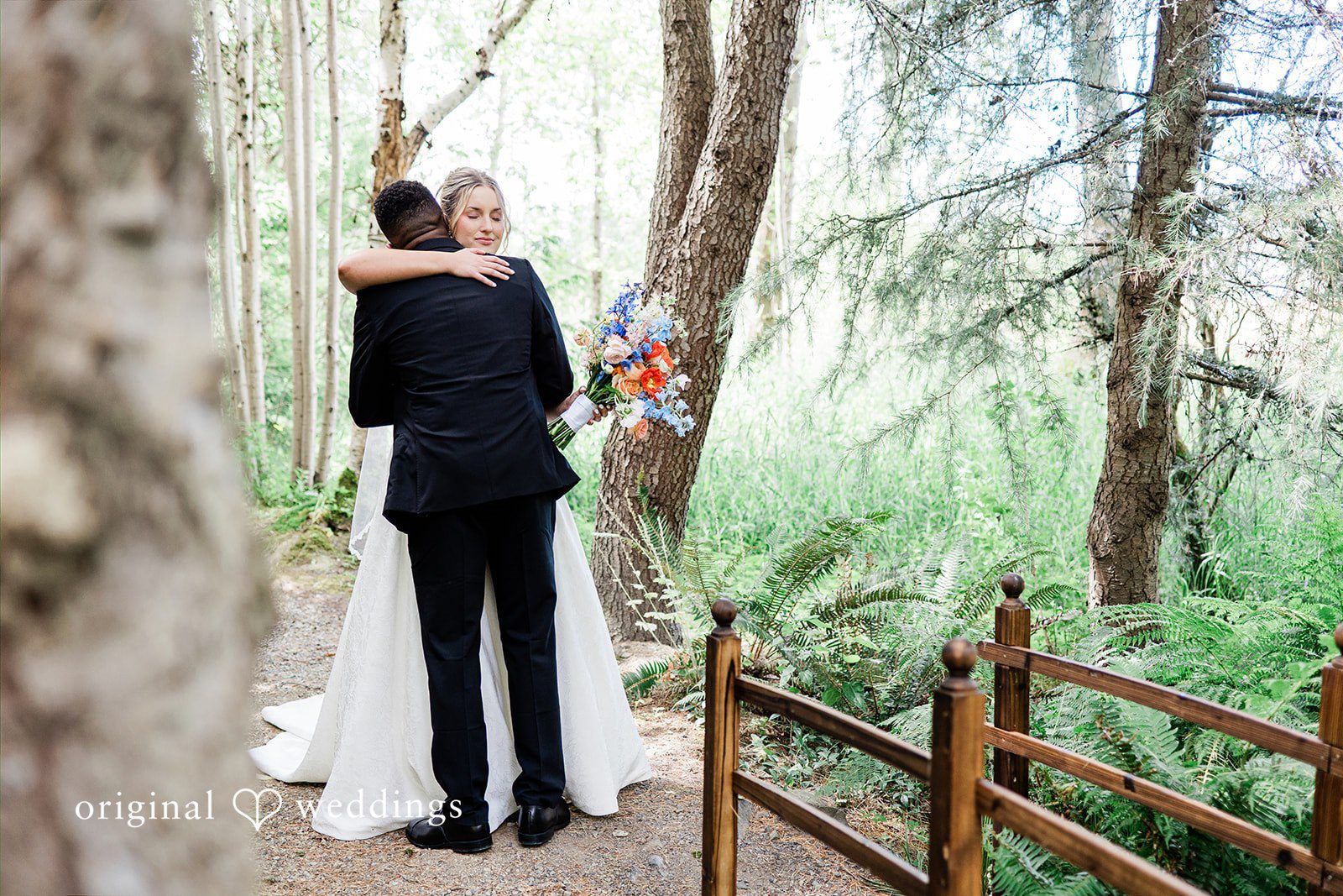 Katrina + Japhet Bride and groom hugging each other while standing on a wooden walkway in a forest.