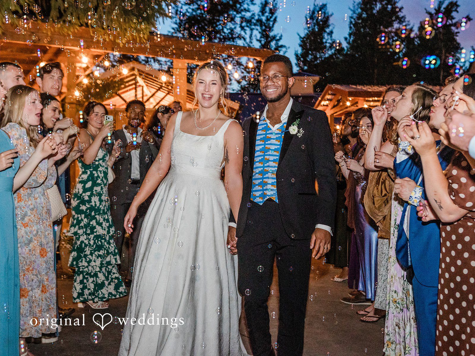 Katrina + Japhet Bride and groom walking hand-in-hand down a path while wedding guests stand on both sides cheering.