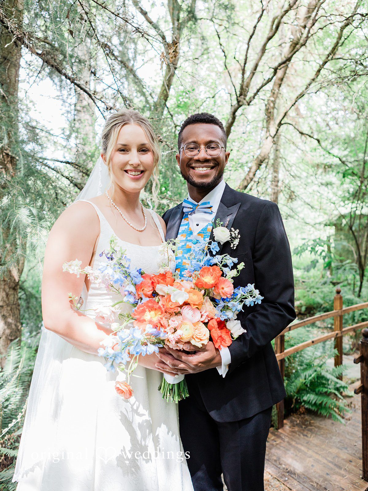 Katrina + Japhet Bride and groom smiling at the camera while holding a vibrant orange and blue bouquet.