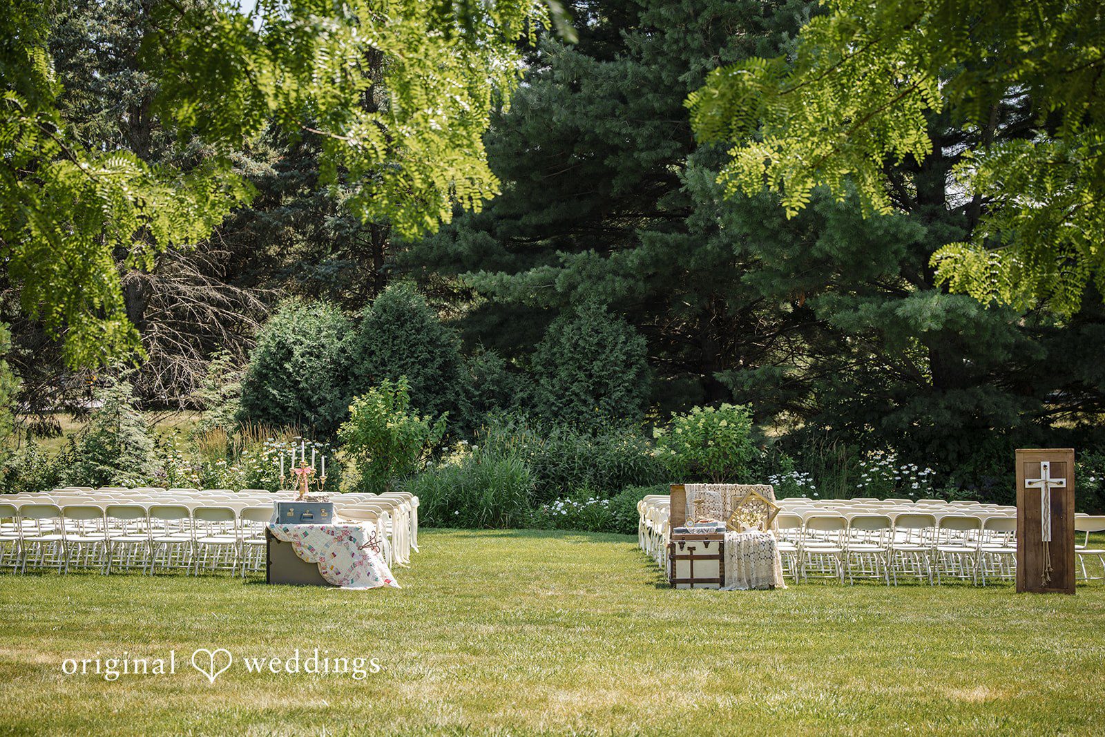 A wide shot reveals an empty ceremonial setup in a grassy field bordered by thick woods.