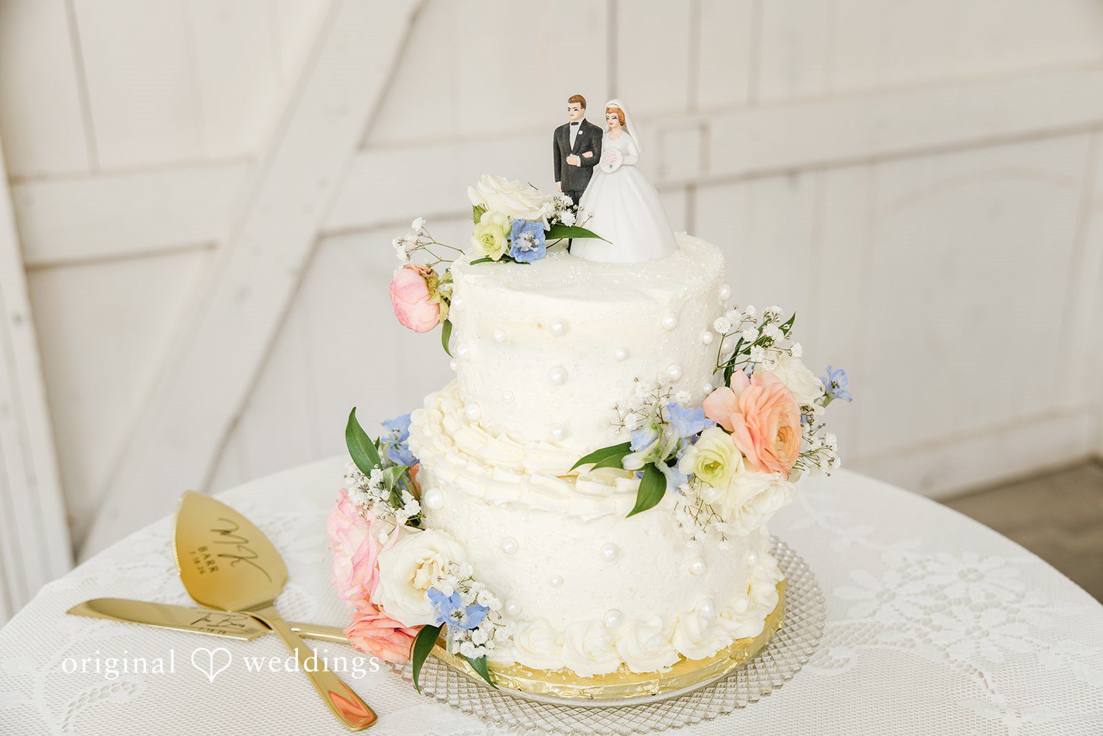 A three-tiered white wedding cake adorned with delicate floral patterns rests on a table.