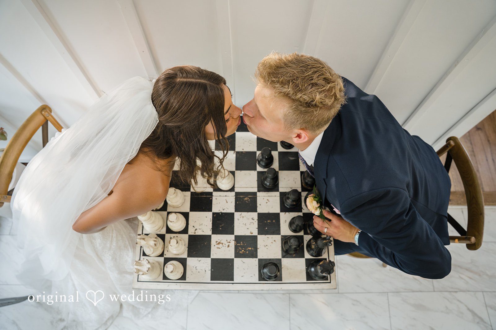 A bride and groom kissing each other over a chessboard layout.
