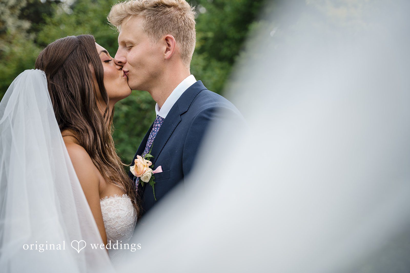 A close-up view focuses on a bride and groom hidden behind the sheer fabric of a white wedding veil.