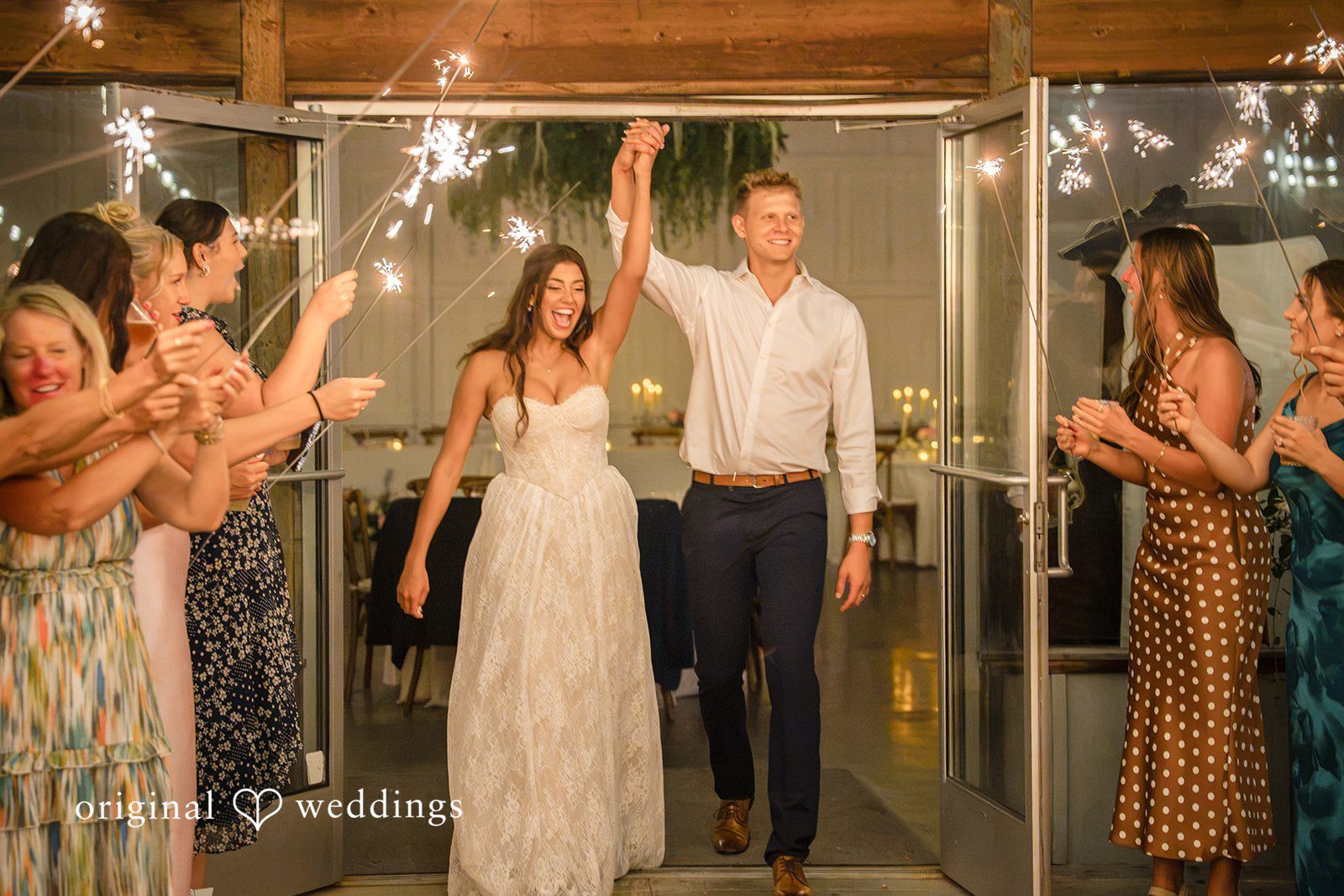 A bride walks through a crowd of guests holding up glowing sparklers during a grand exit.