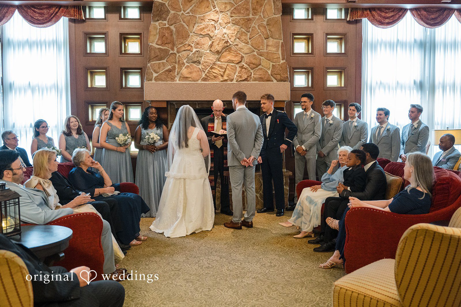 Ava + Zach A wide shot of a wedding ceremony in front of a stone fireplace.