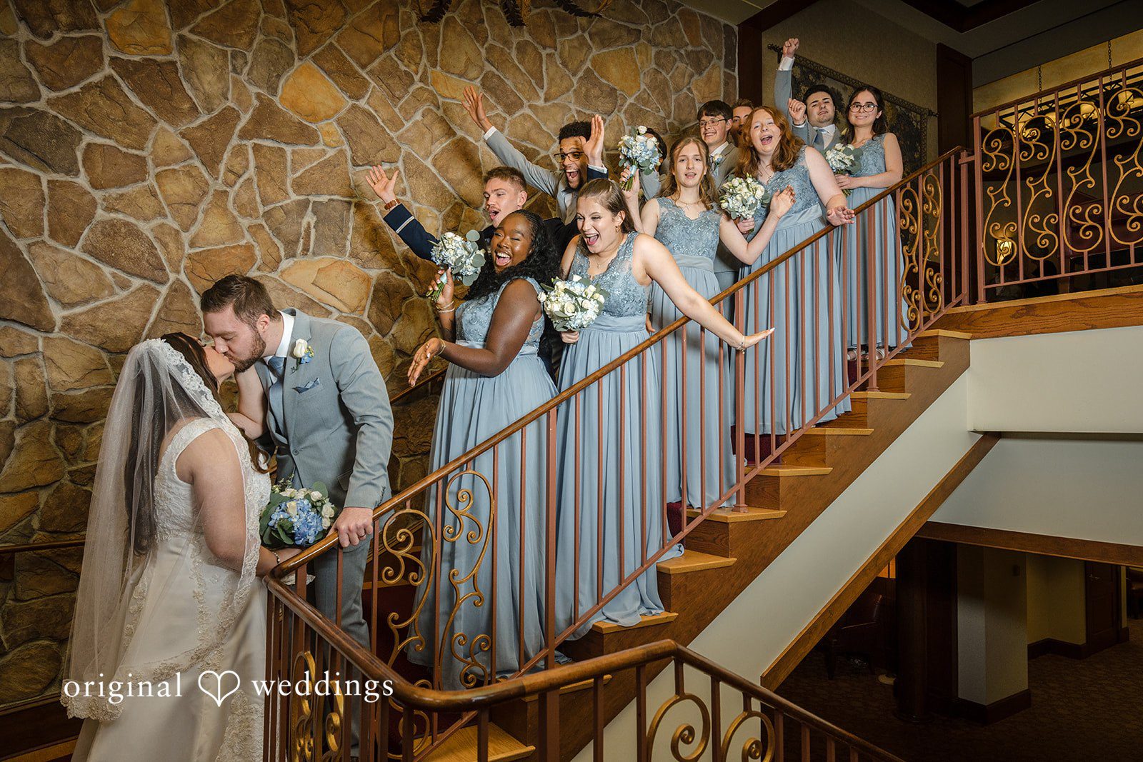 Ava + Zach A large group of bridesmaids in matching blue dresses posing on a staircase.