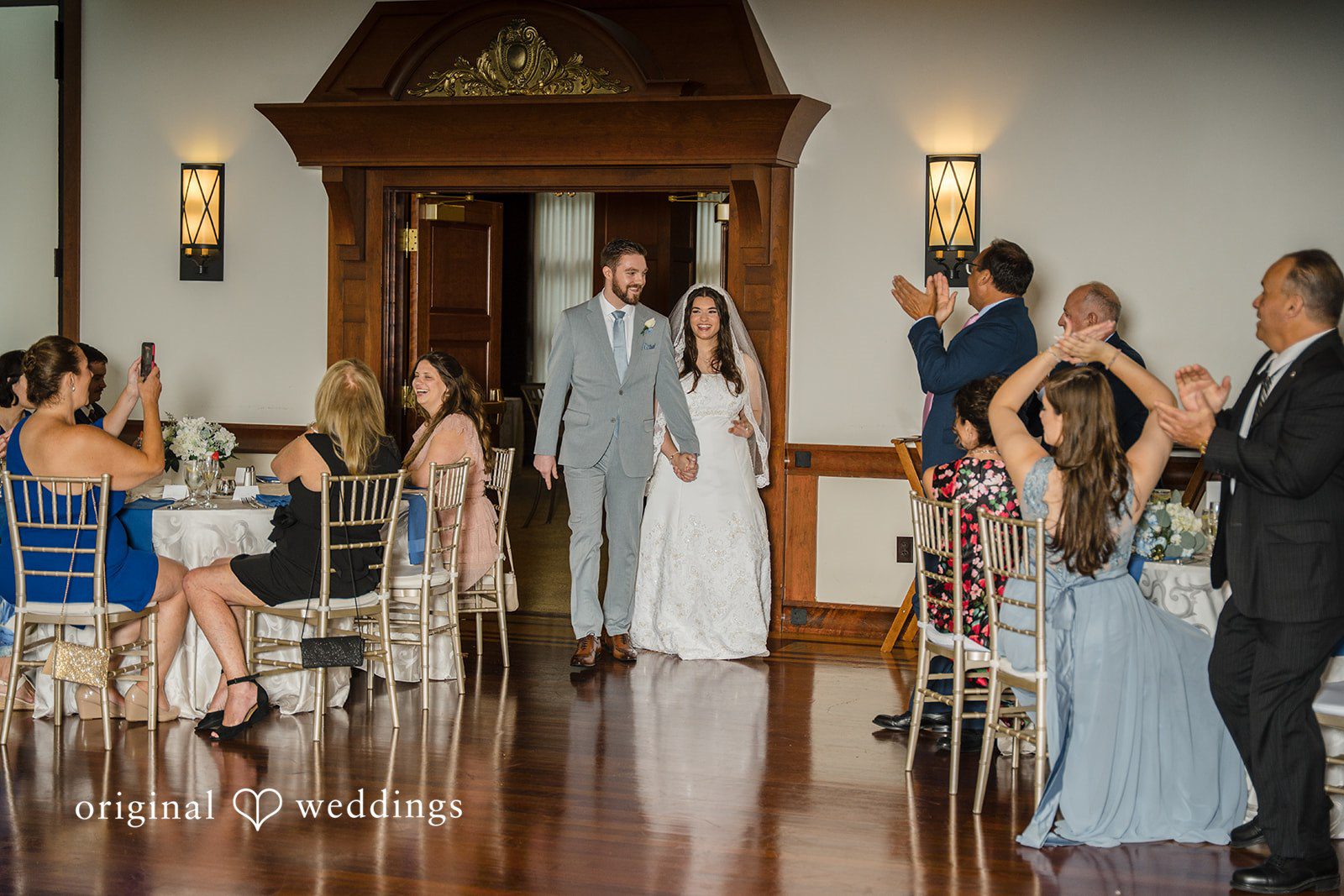 Ava + Zach A bride and groom entering their wedding reception as guests clap and cheer.