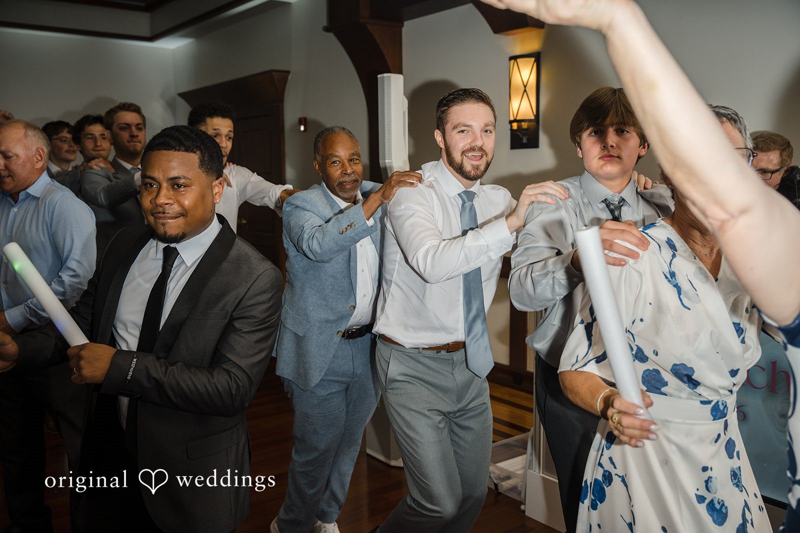 Ava + Zach Wedding guests smiling and laughing while forming a conga line on the dance floor during a reception.
