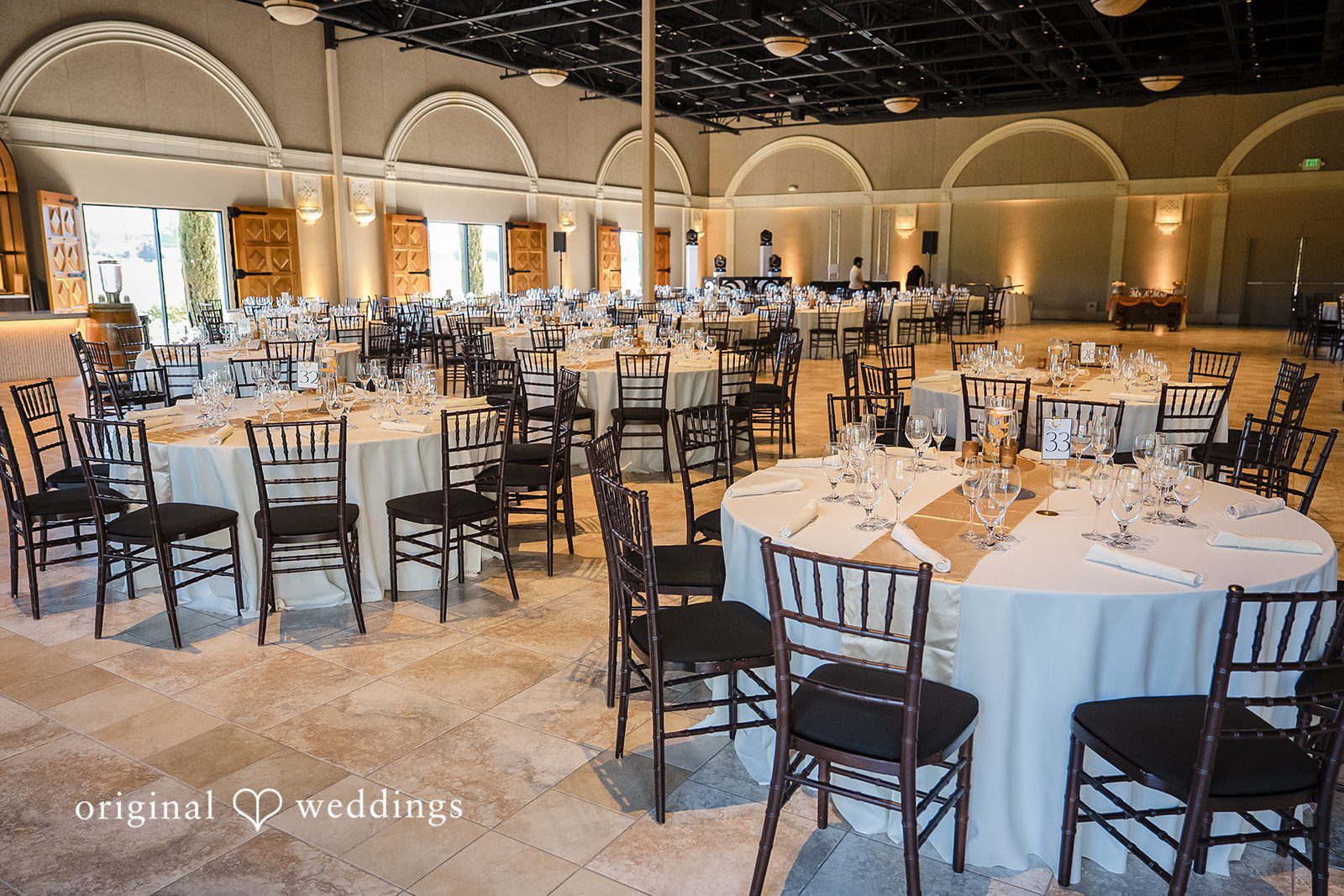 Kathir + Nandita A large banqueting hall arranged with round tables and white linens.