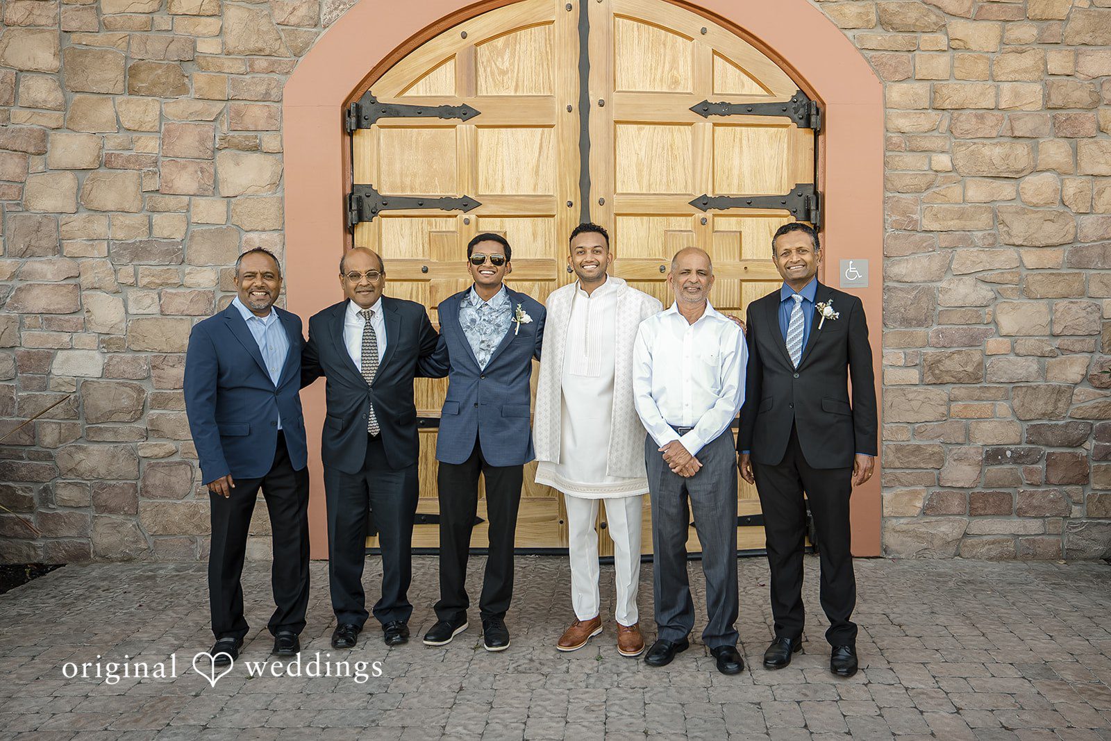 Kathir + Nandita A groom and group of five men posing together in a mix of formal suits and traditional attire.
