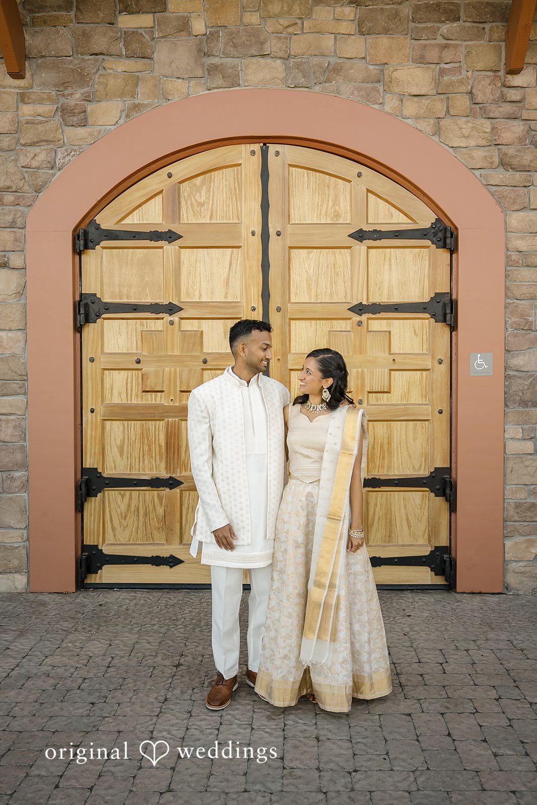 Kathir + Nandita A bride and groom posing together in coordinated white traditional wedding garments.