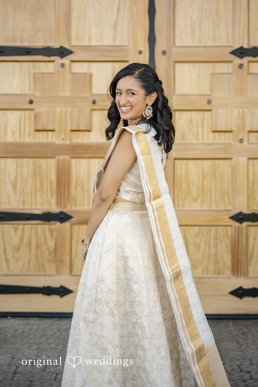 Kathir + Nandita A woman smiling while posing in an elegant white and gold traditional dress.