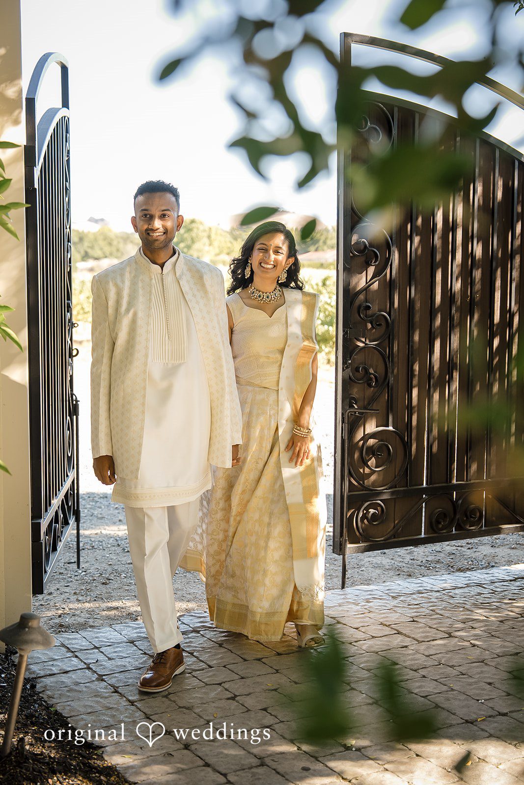 Kathir + Nandita A bride and groom walking hand-in-hand through a stone archway.