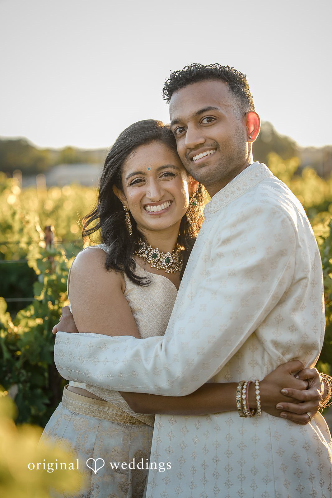 Kathir + Nandita A man embracing a smiling woman during a portrait session in a vineyard.
