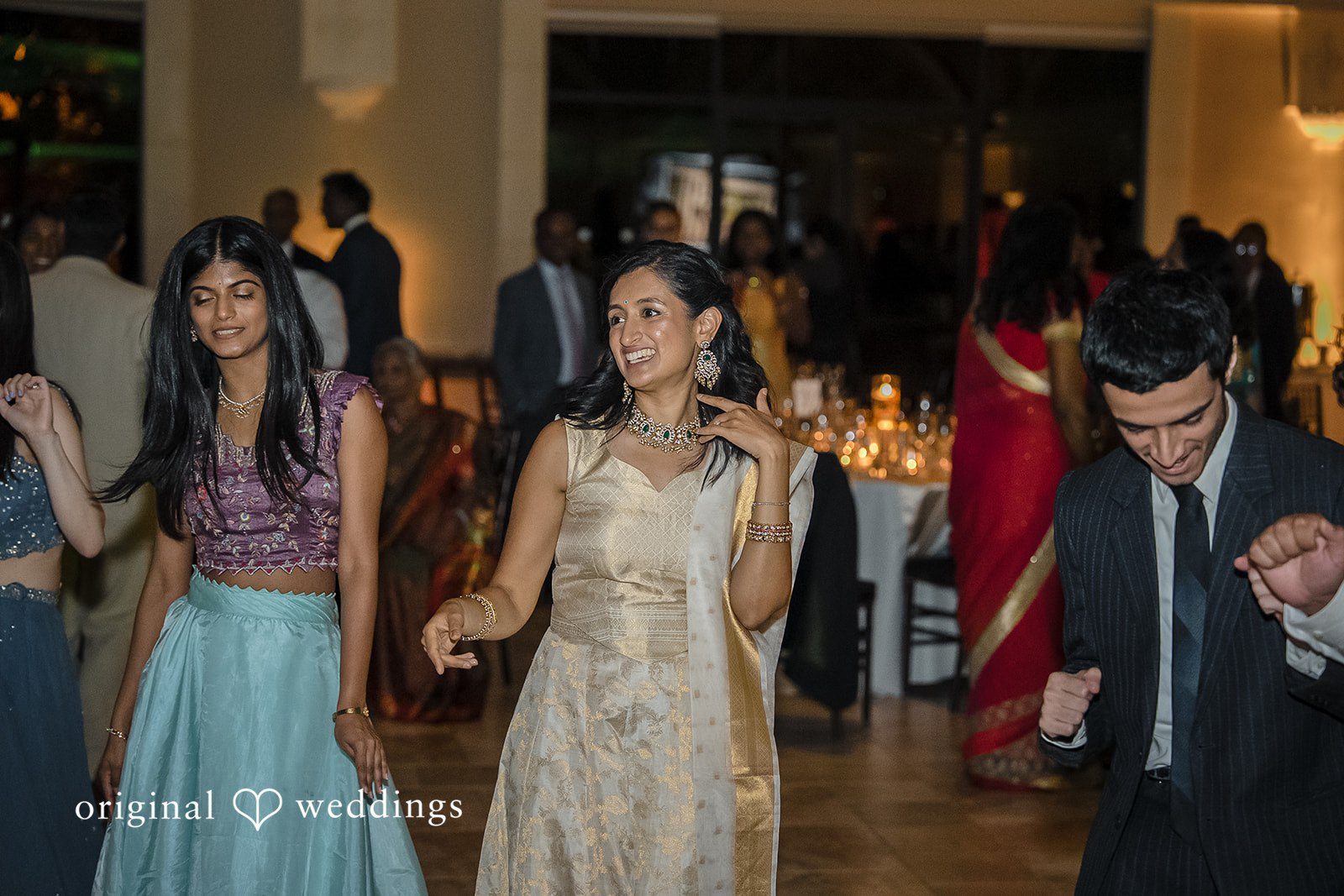 Kathir + Nandita A bride in a traditional dress dancing among guests at a reception.