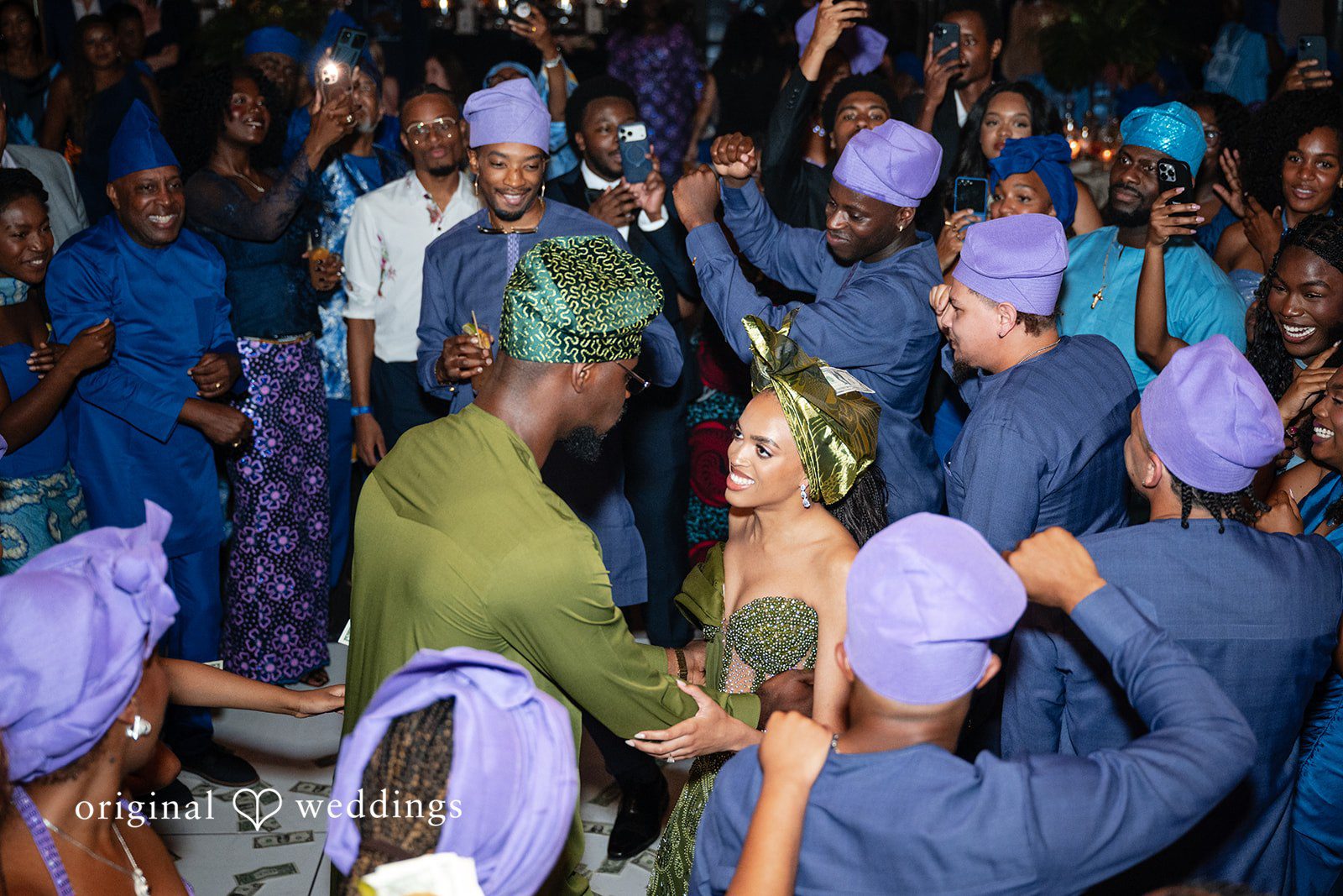 A man in a green outfit dances among a large crowd of wedding guests wearing vibrant blue traditional clothing.