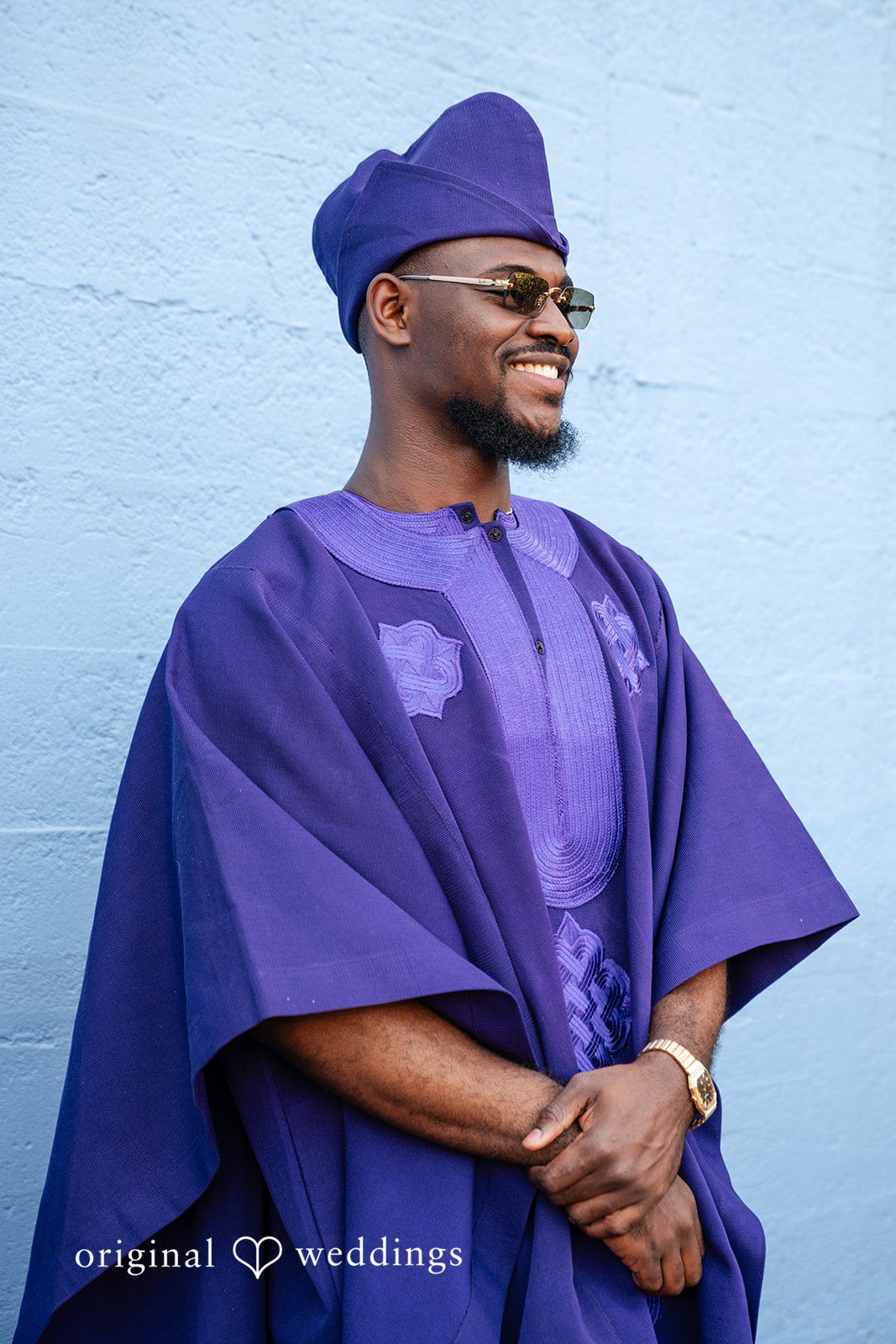 A smiling man wearing a traditional purple Agbada garment and matching cap.