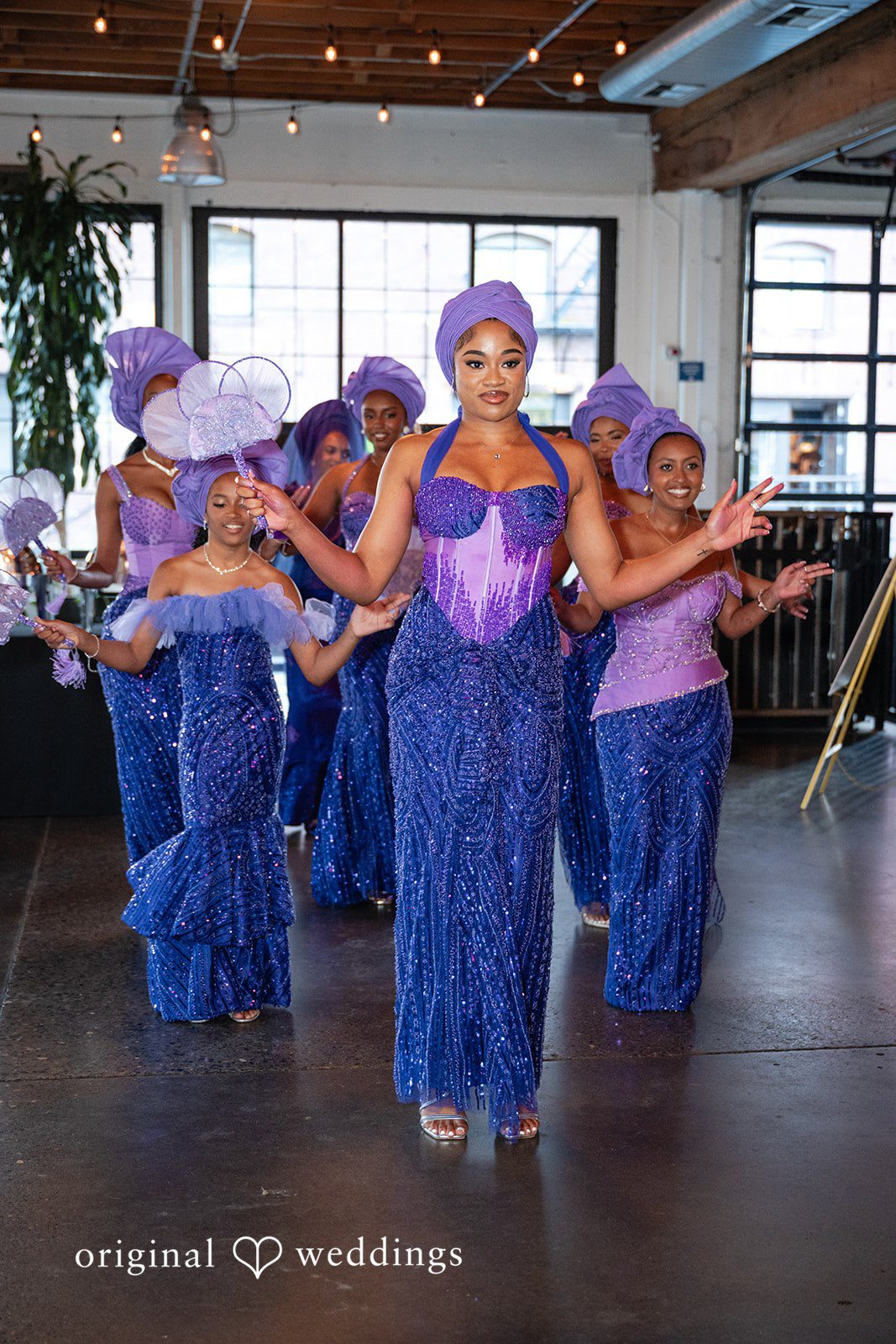A group of women wearing blue dresses and traditional headwraps dancing together.