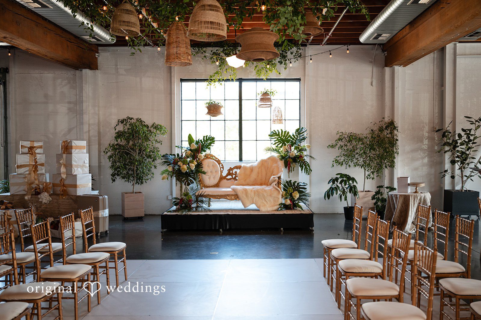 An empty event space lined with wooden chairs and decorated with lush greenery.