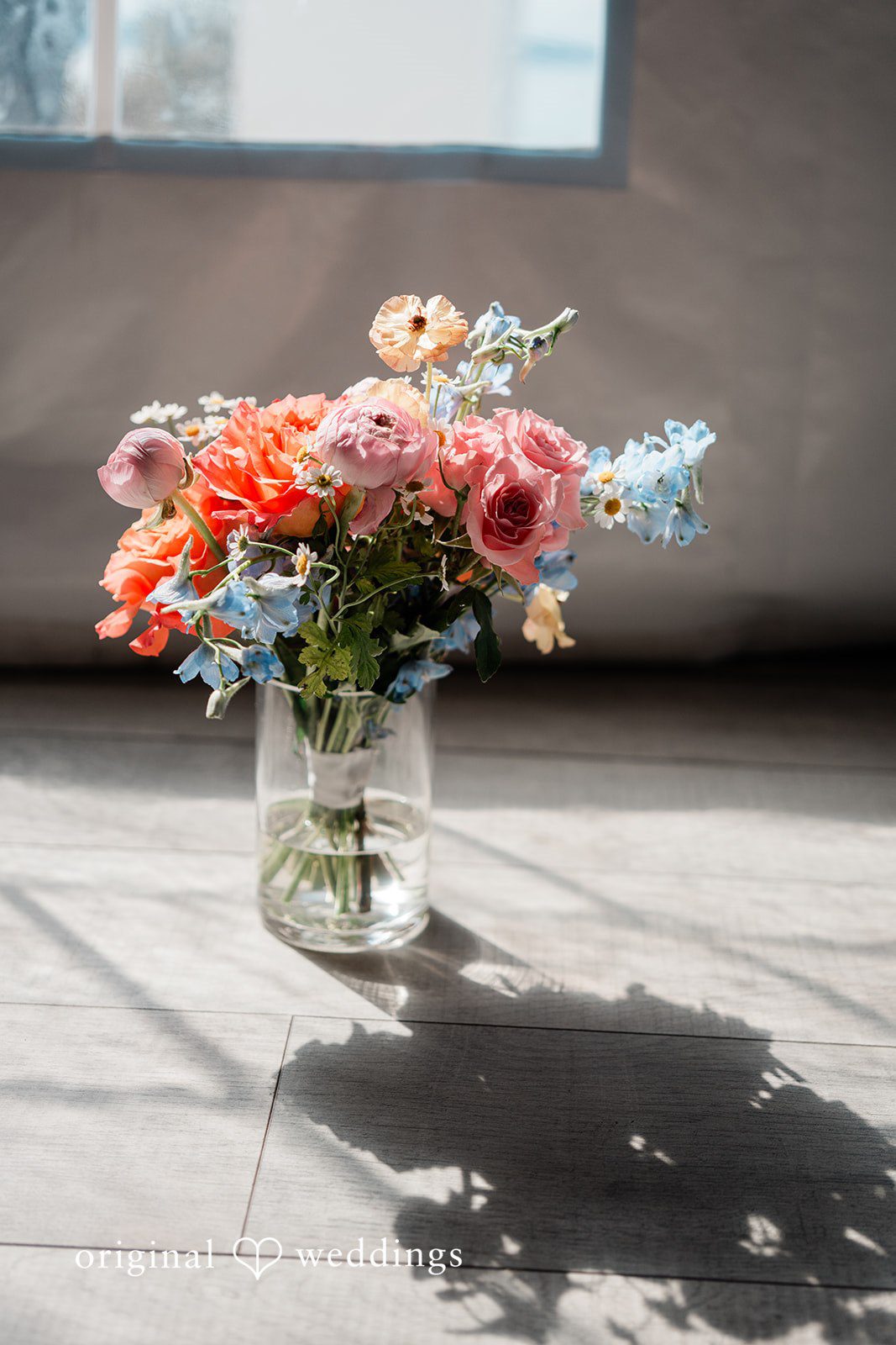 Katie + Gerald A vibrant bouquet of pink, orange, and blue wildflowers arranged in a glass vase.