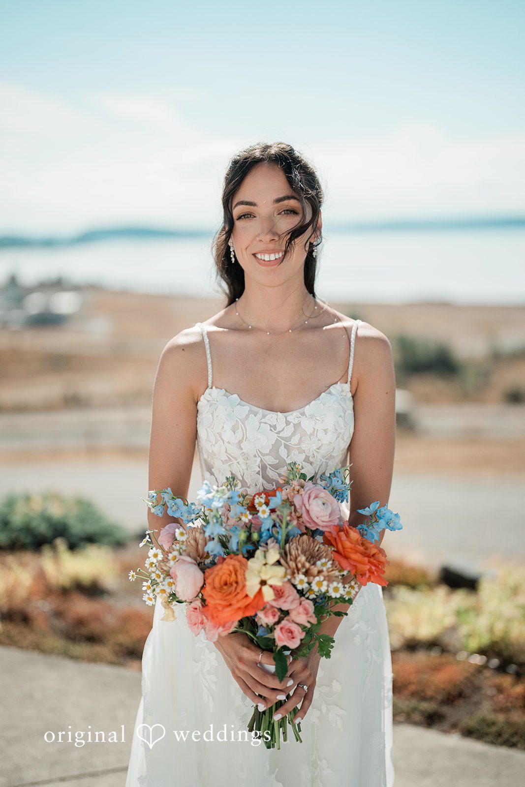 Katie + Gerald A smiling bride wearing a white gown and holding a colorful flower bouquet.