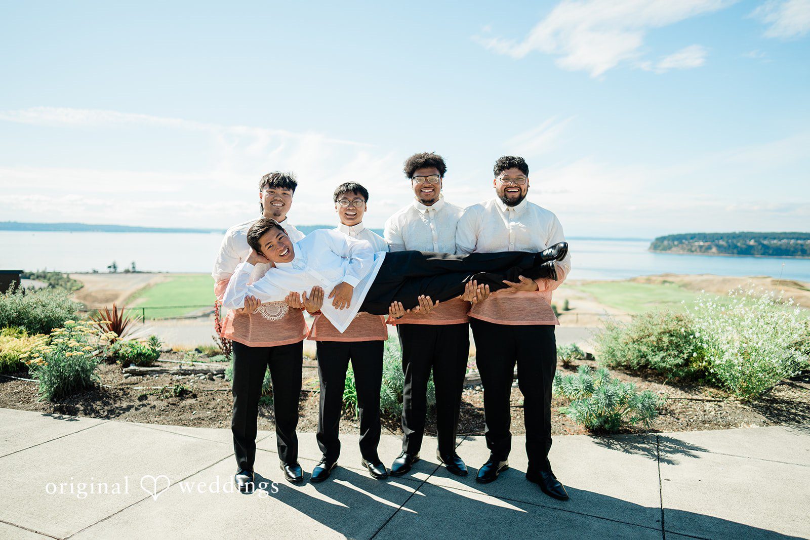 Katie + Gerald A wedding party standing in a line along a scenic waterfront overlook.