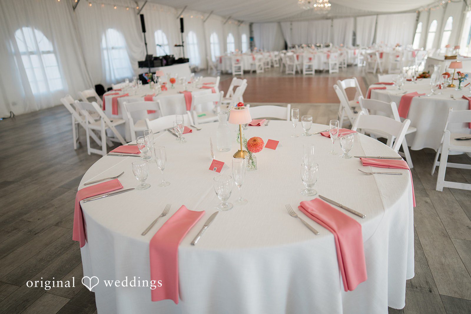 Katie + Gerald A close-up of a round reception table set with white tablecloths and pink napkins.