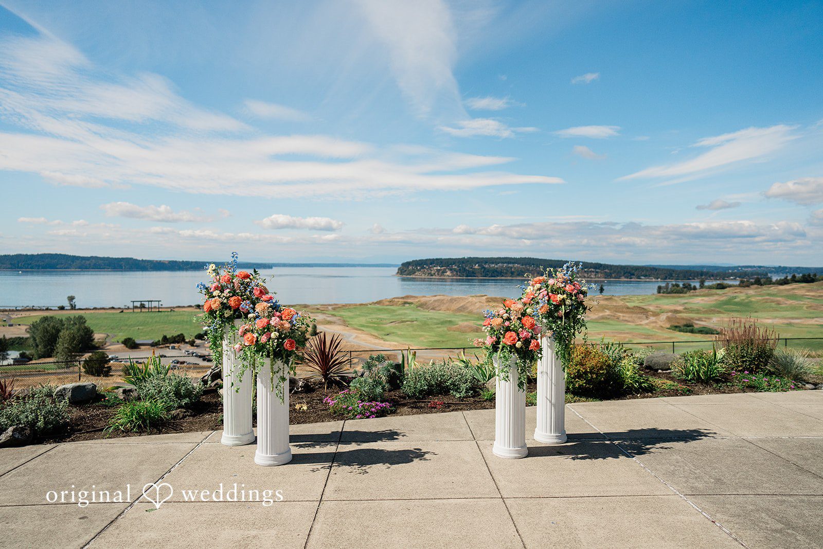 Katie + Gerald An oceanfront wedding ceremony setup with two floral arrangements on wooden pillars.