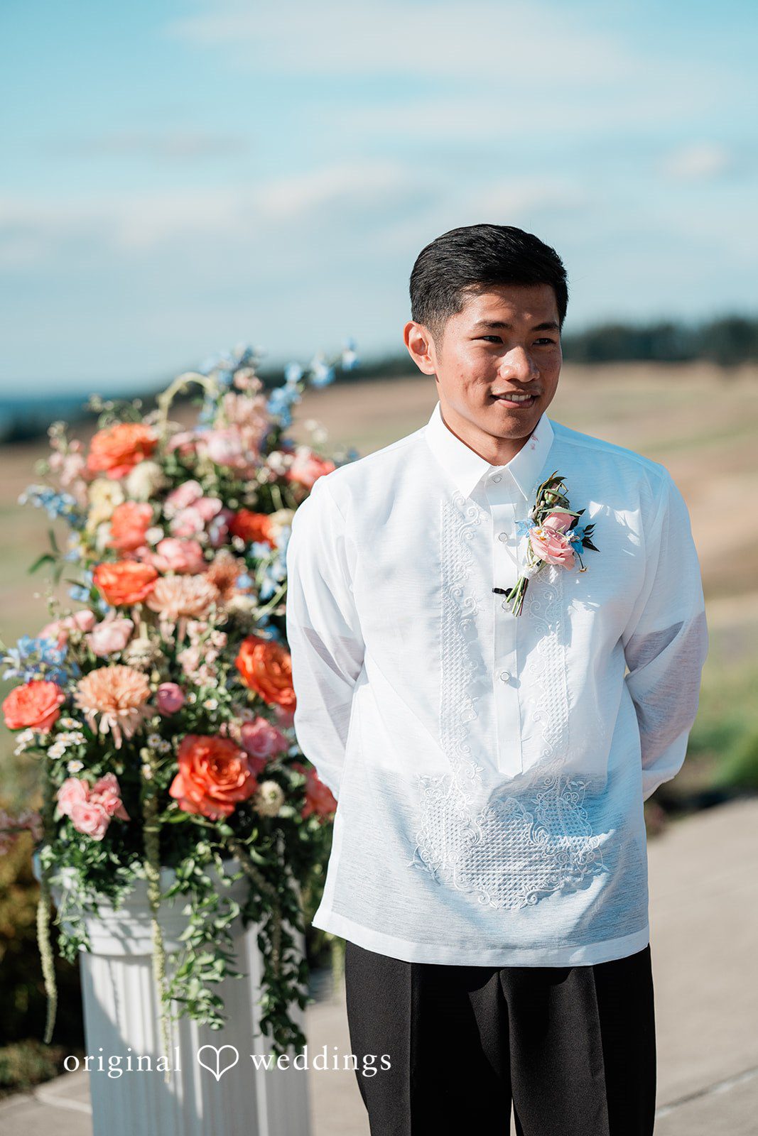 Katie + Gerald A portrait of a groom smiling next to a vibrant orange floral display.