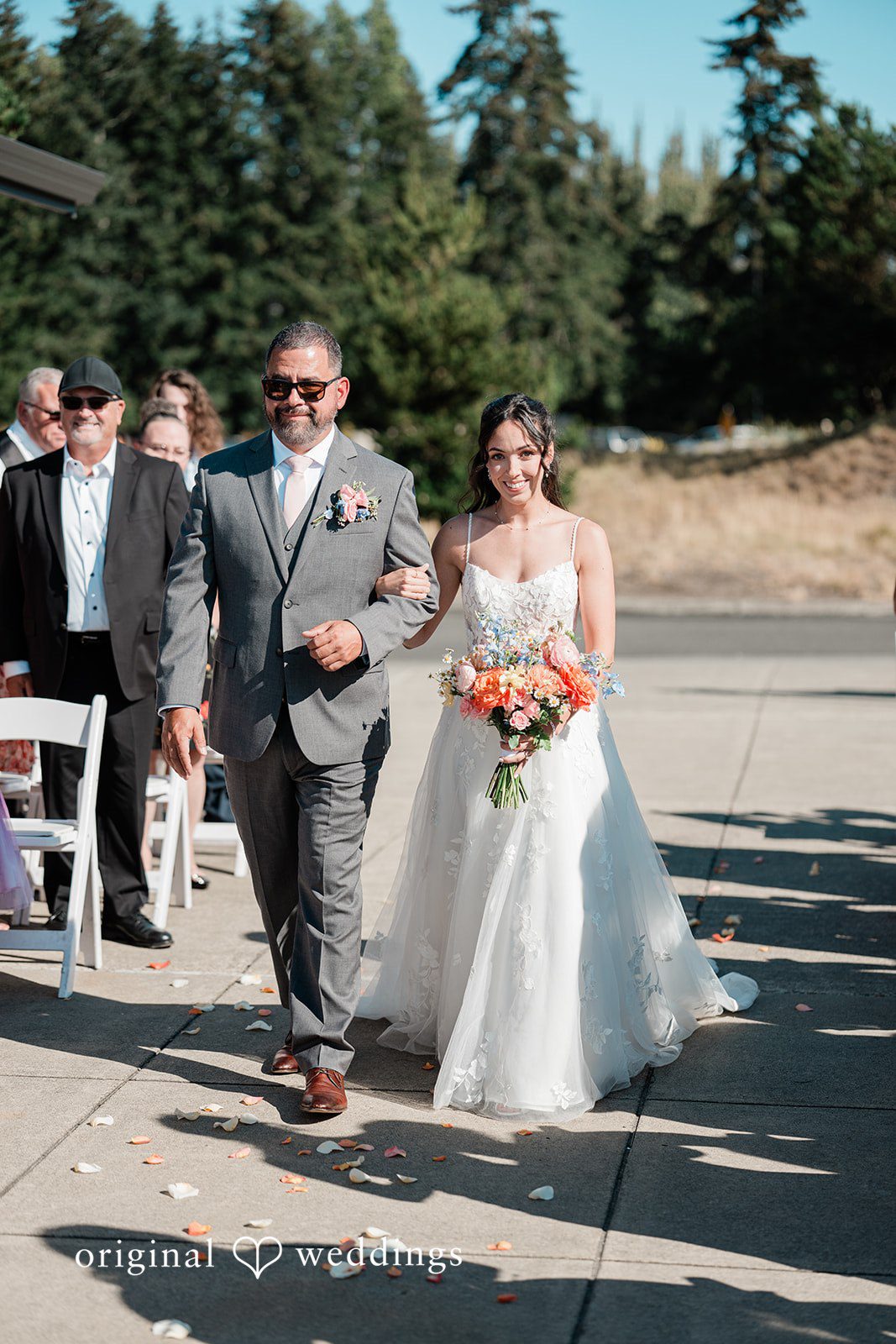Katie + Gerald A bride and man walking down a paved path while guests look on.