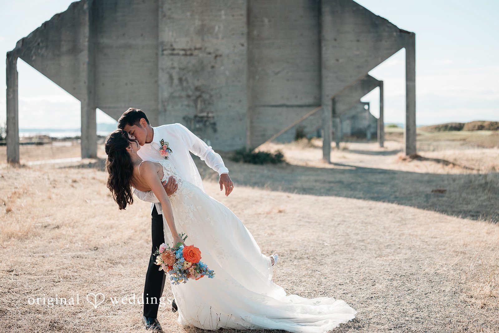 Katie + Gerald A bride and groom sharing a kiss in front of a rustic concrete structure.