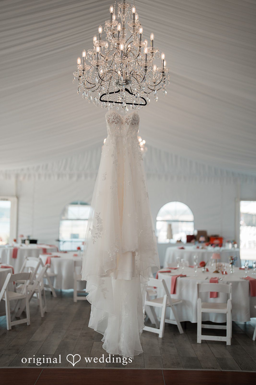 Katie + Gerald A white wedding dress hanging from a crystal chandelier in a reception space.