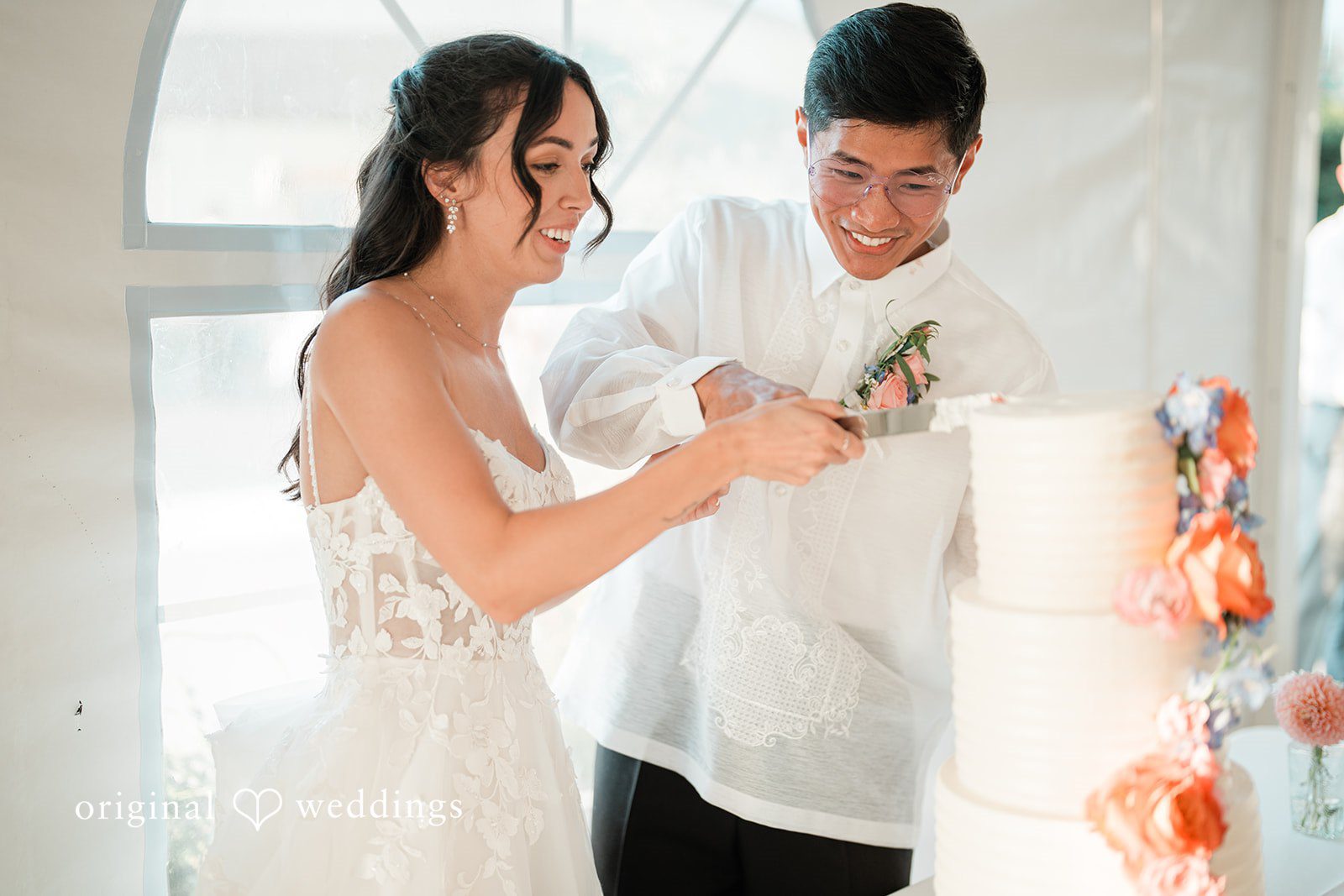 Katie + Gerald A bride and groom standing next to their multi-tiered white wedding cake.