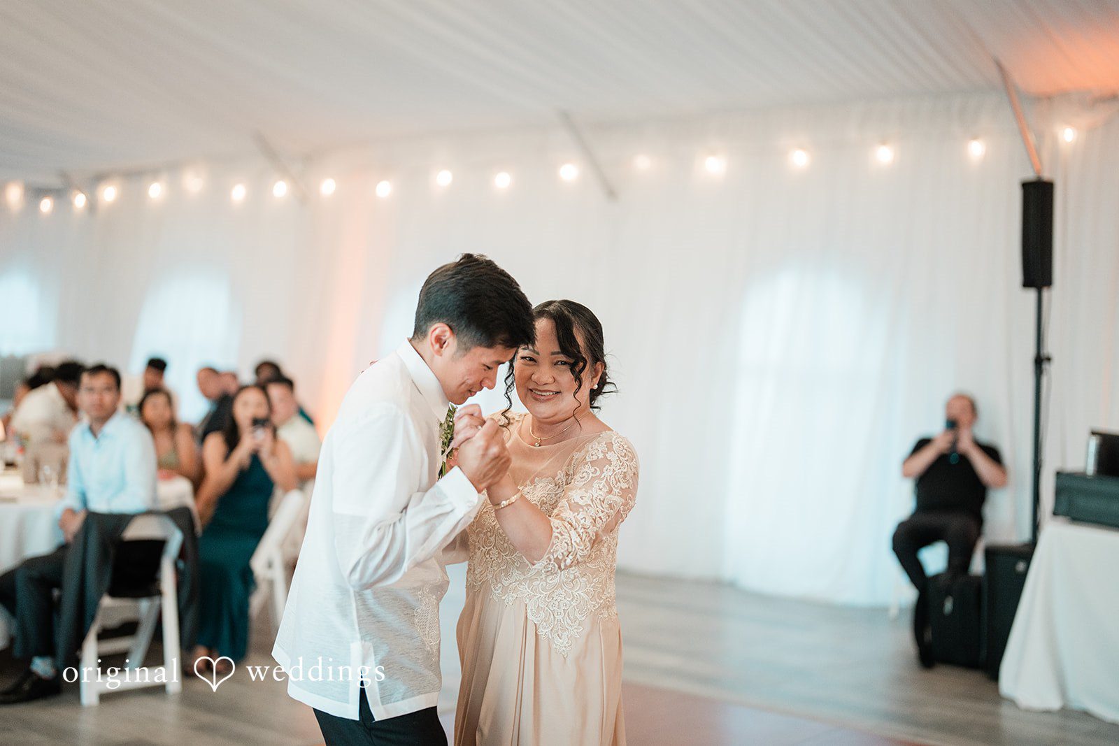 Katie + Gerald A women and groom dancing together through a brightly lit reception room.
