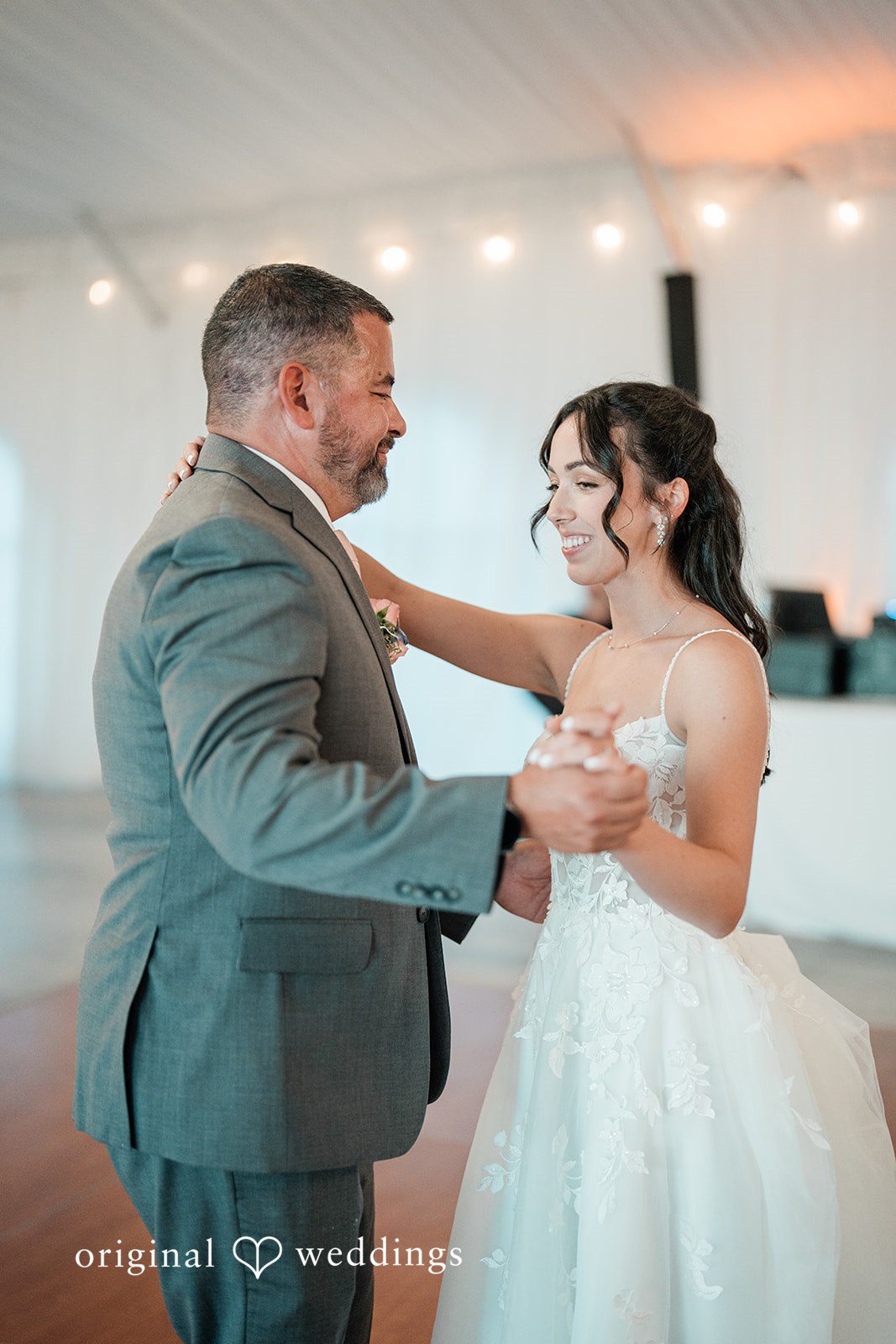 Katie + Gerald A bride and a man in a grey suit smiling while sharing a dance.