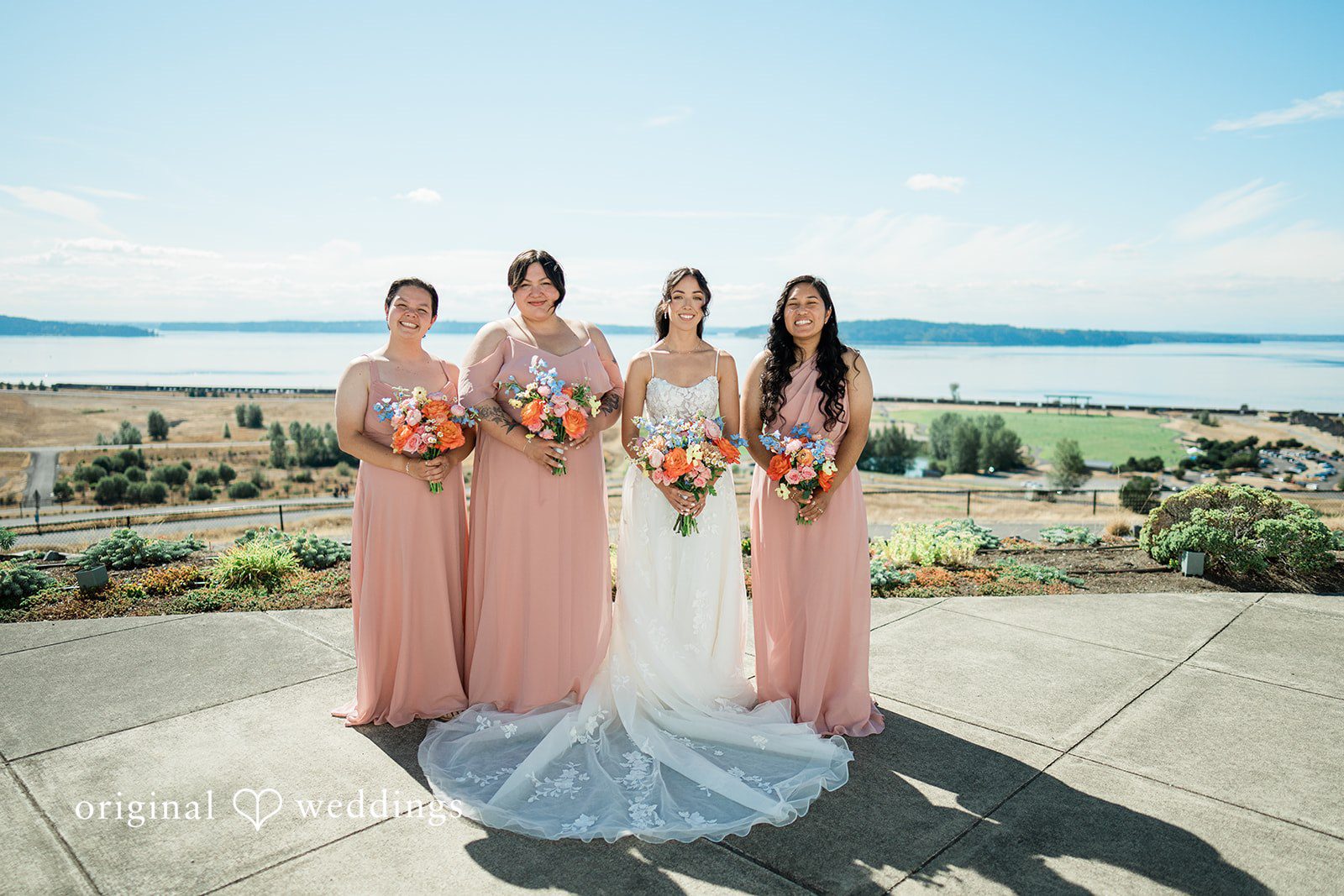 Katie + Gerald A wedding party posing together on a coastal pathway with the ocean in the background.