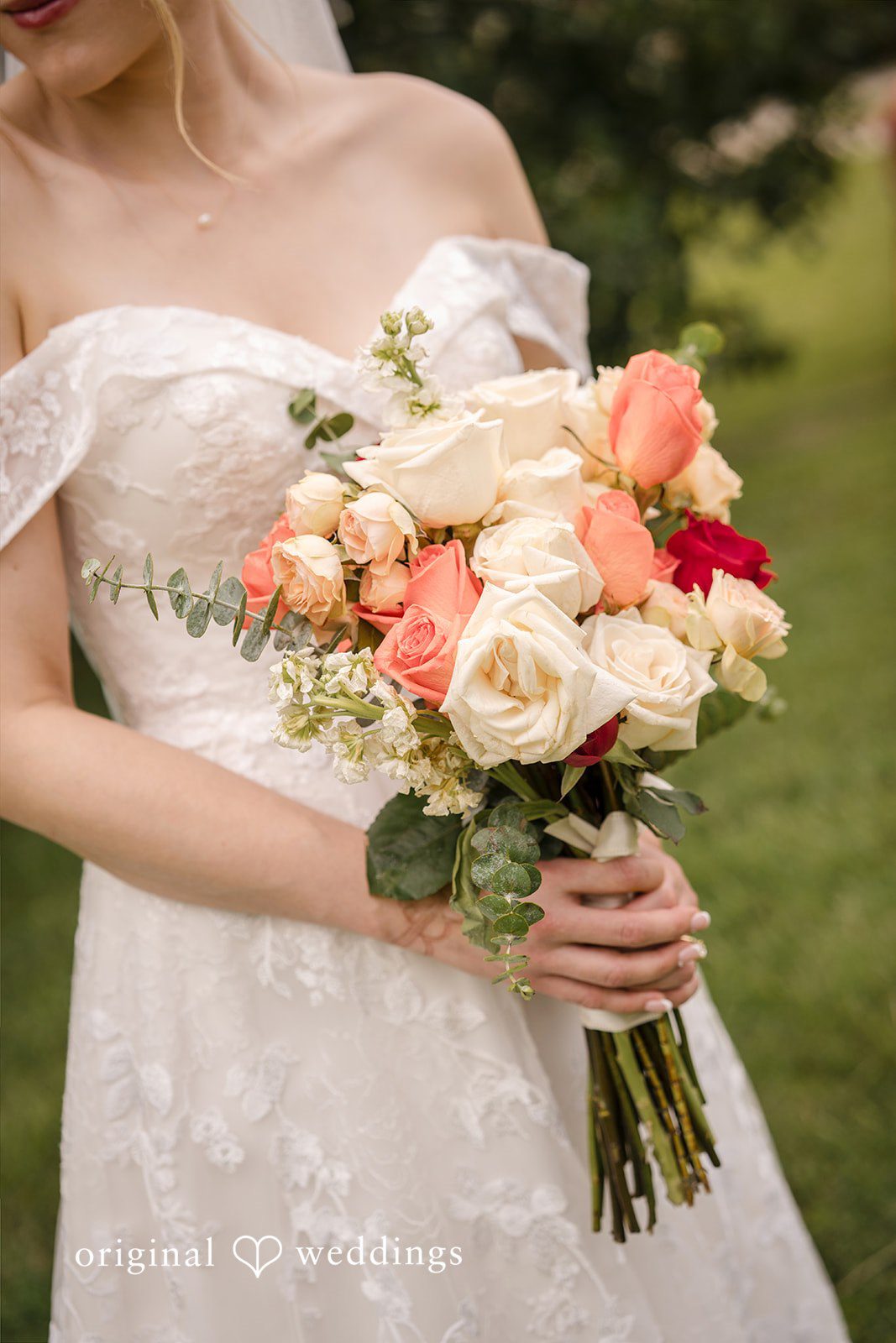 Julie + Joshua A close-up of a bride holding a large bouquet of white, pink, and peach roses.