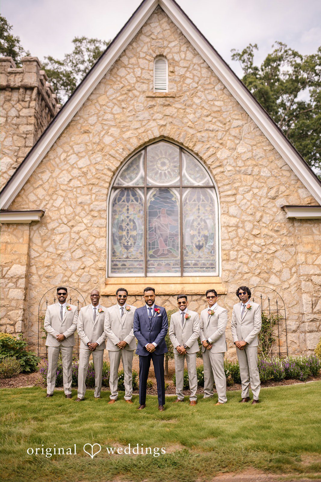 Julie + Joshua A groomsmen posing together in front of a stone church building.