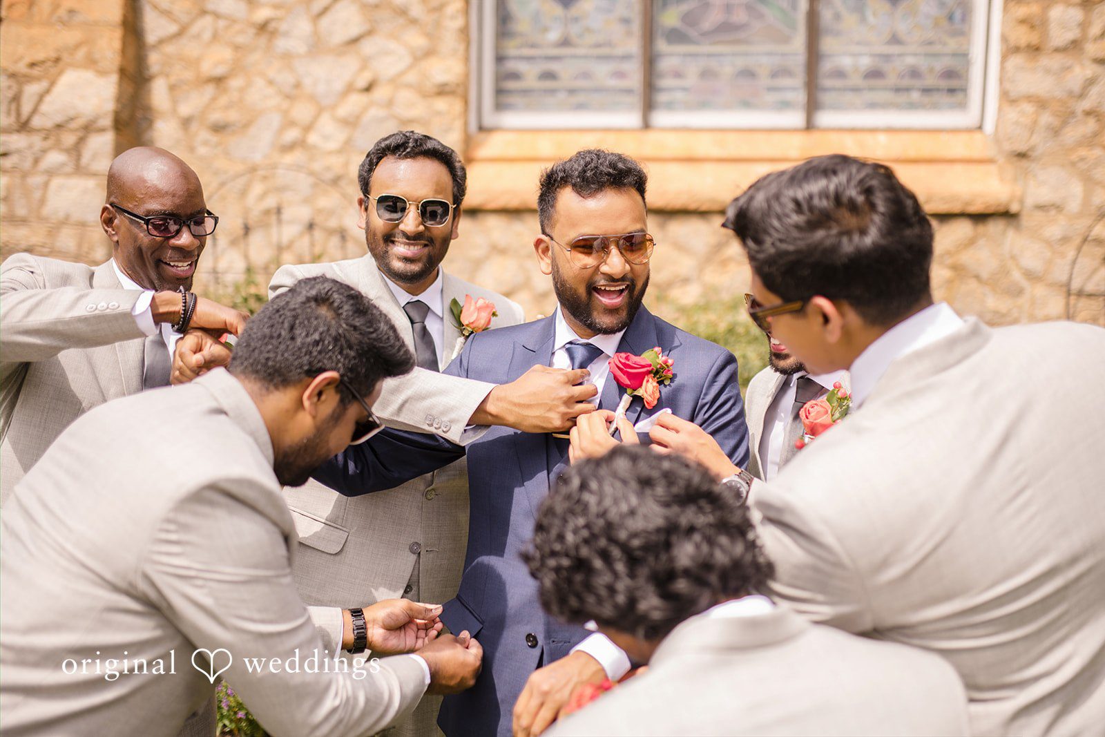 Julie + Joshua A groom laughing while getting ready surrounded by his groomsmen.
