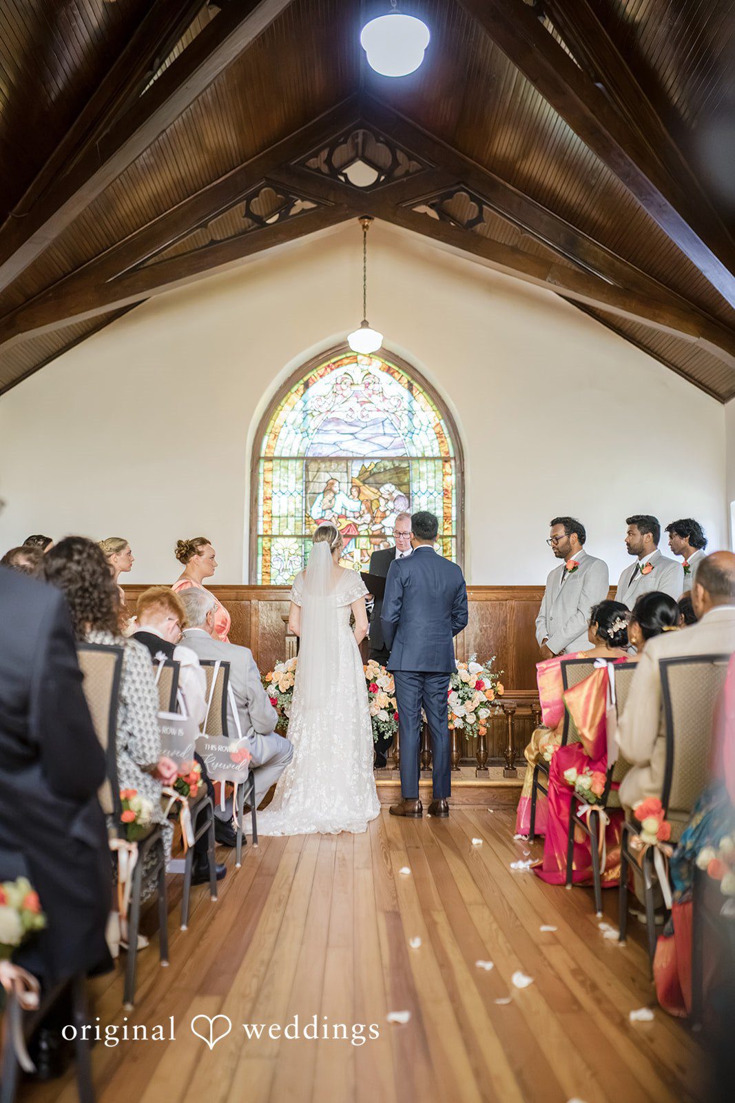 Julie + Joshua A bride walking down the aisle of a chapel filled with seated guests.