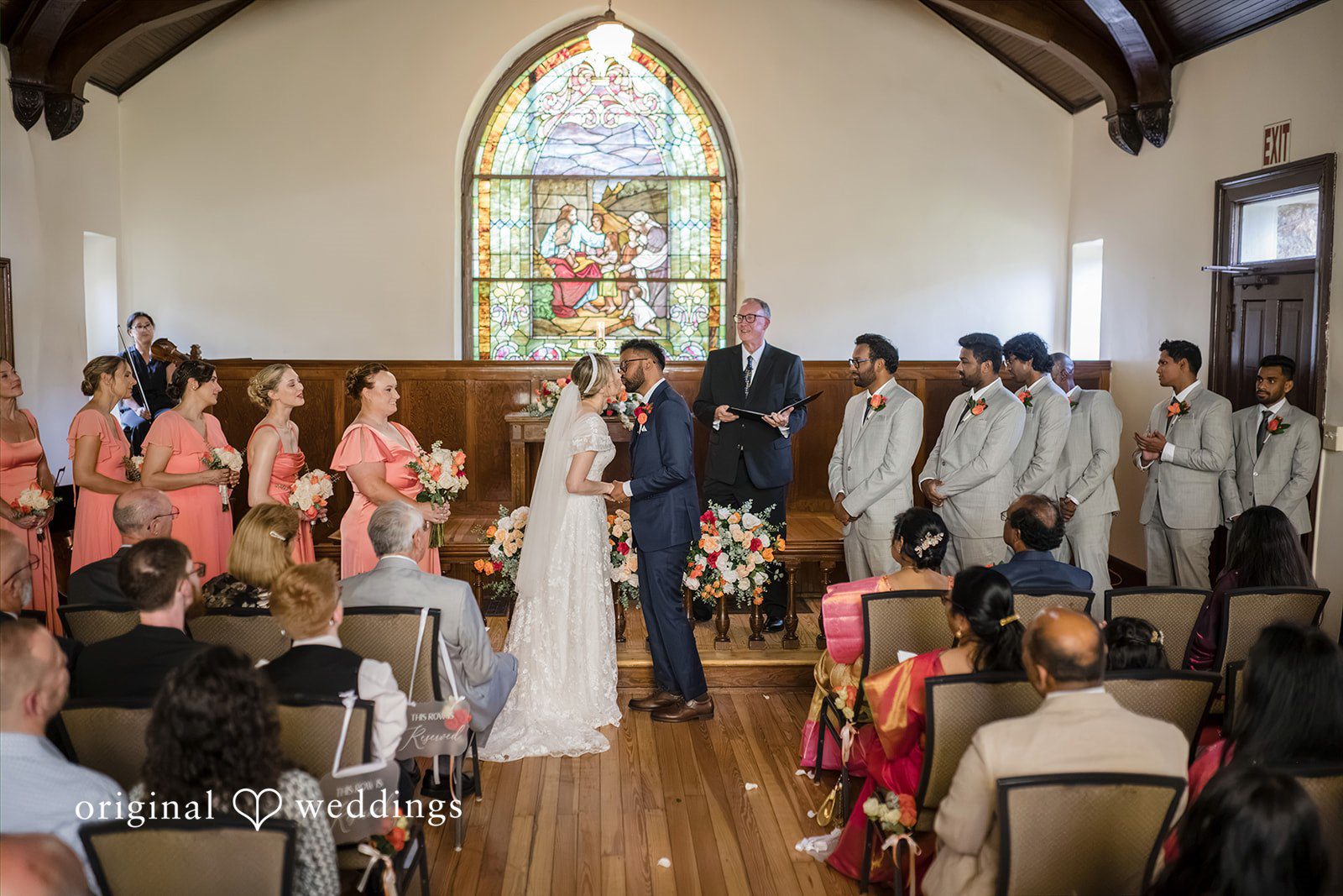 Julie + Joshua A wide shot of the wedding ceremony inside a chapel filled with guests.