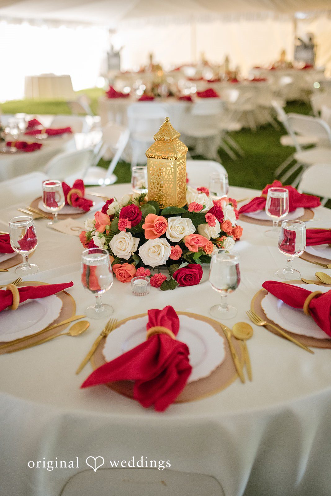 Julie + Joshua A round reception table set with white linens, red napkins, and a floral centerpiece.