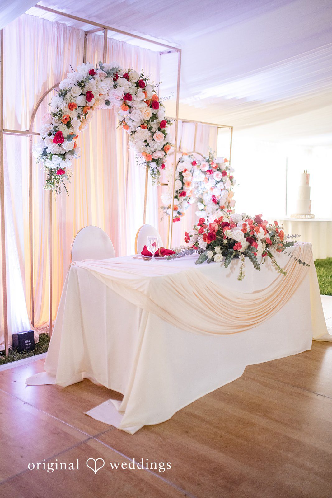 Julie + Joshua A long head table decorated with white drapery and soft pink floral arrangements.