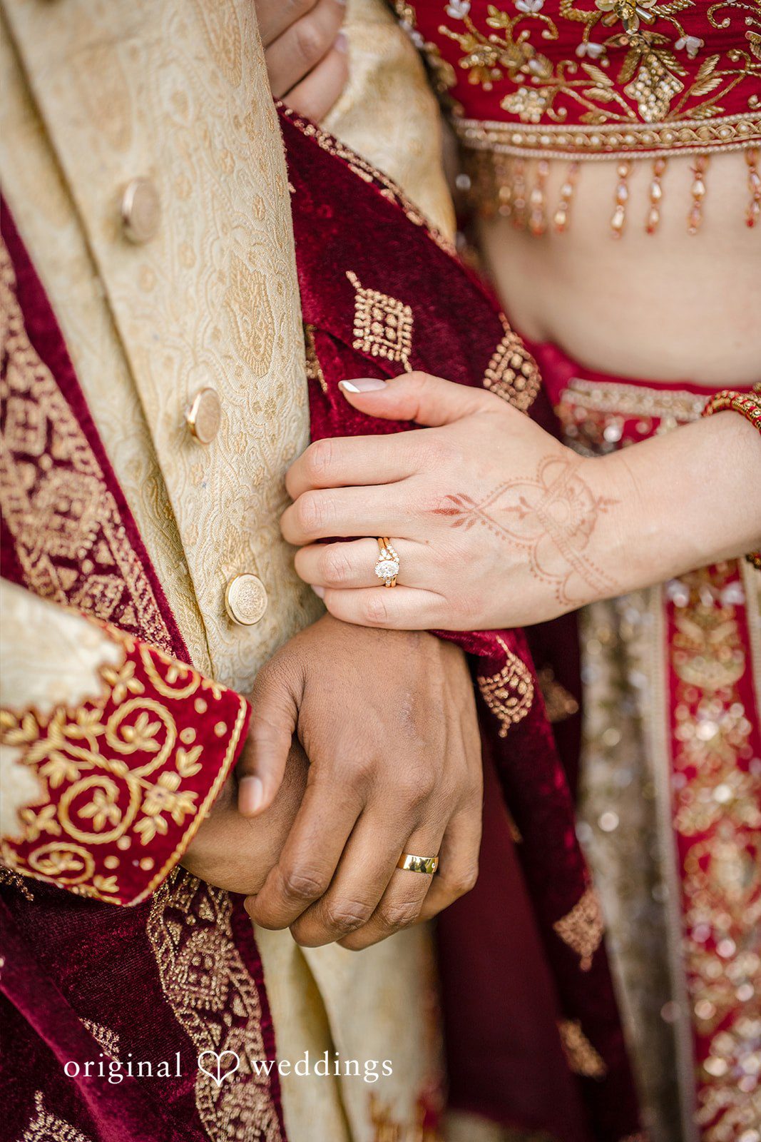 Julie + Joshua A close-up of a bride and groom holding hands over detailed traditional garments.