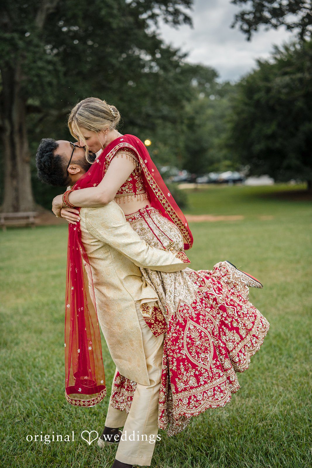 Julie + Joshua A groom carrying his bride in his arms while spinning on a grassy field.