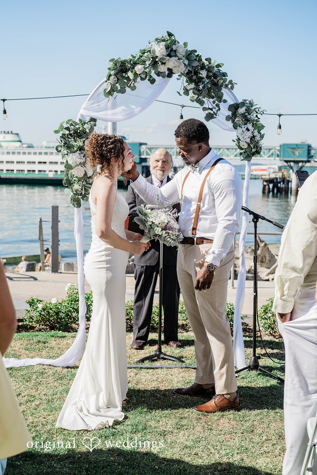 Naomi + Darrell Bride and groom exchanging vows under a floral arch.
