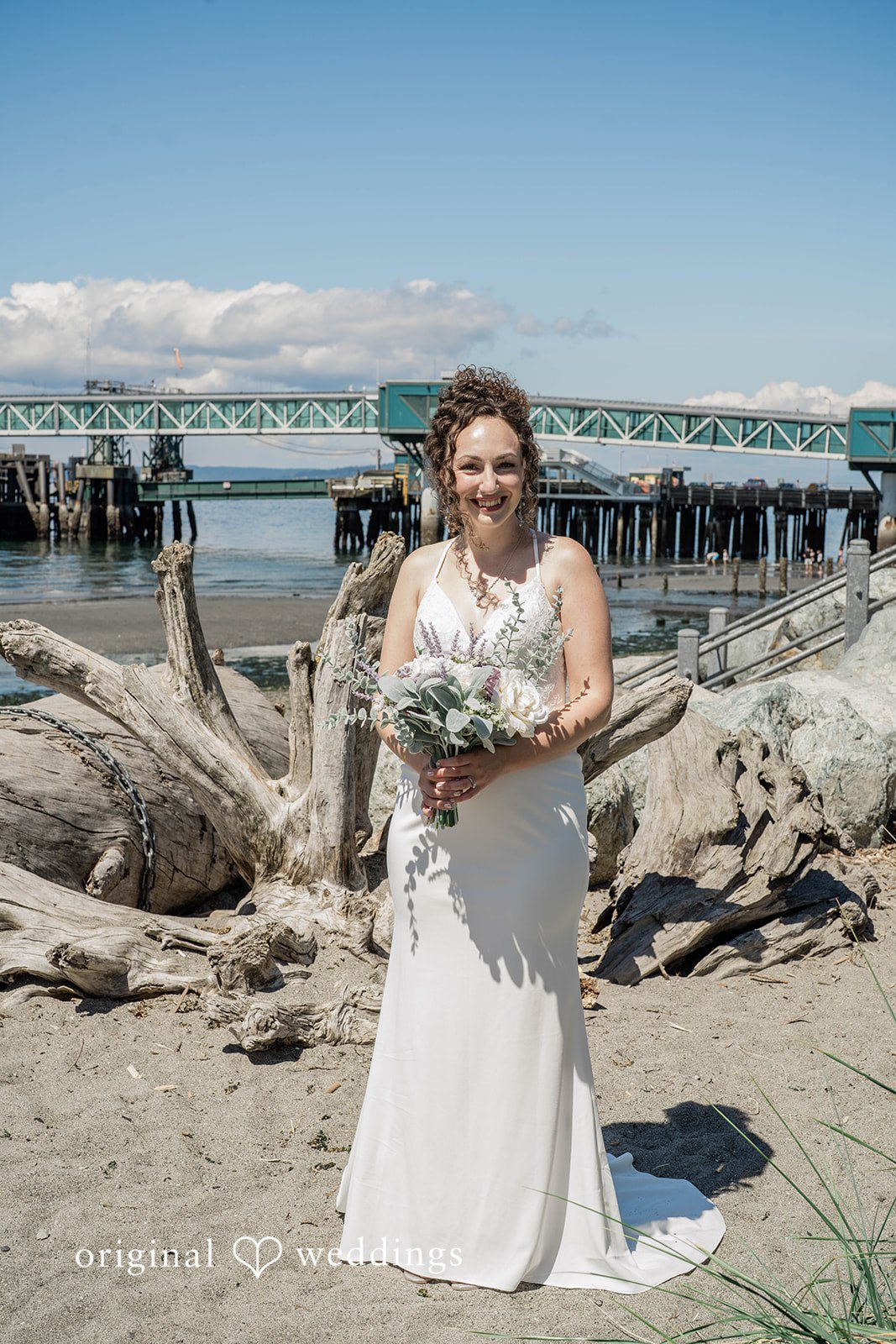 Naomi + Darrell Bride standing alone in a white wedding gown on a wooden deck.